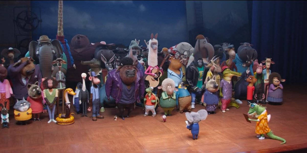 《Sing 2》動物群眾試鏡場景 壁紙 — 一群充滿活力的動畫動物角色穿著色彩繽紛的服裝，在黑暗帷幕下的木製舞台上擺姿勢。