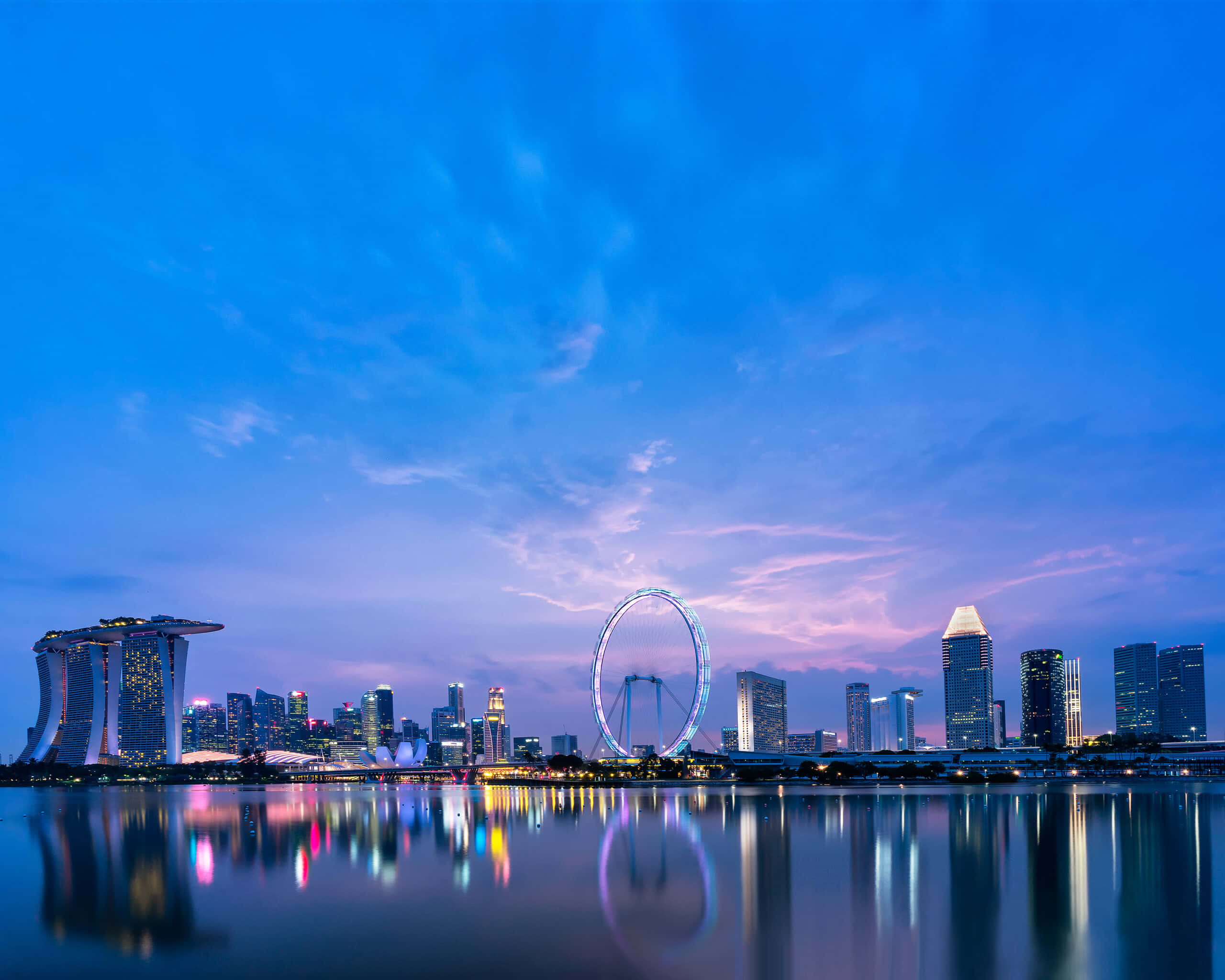 新加坡黃昏城市景觀，燈火通明的建築和摩天輪倒映在水中。