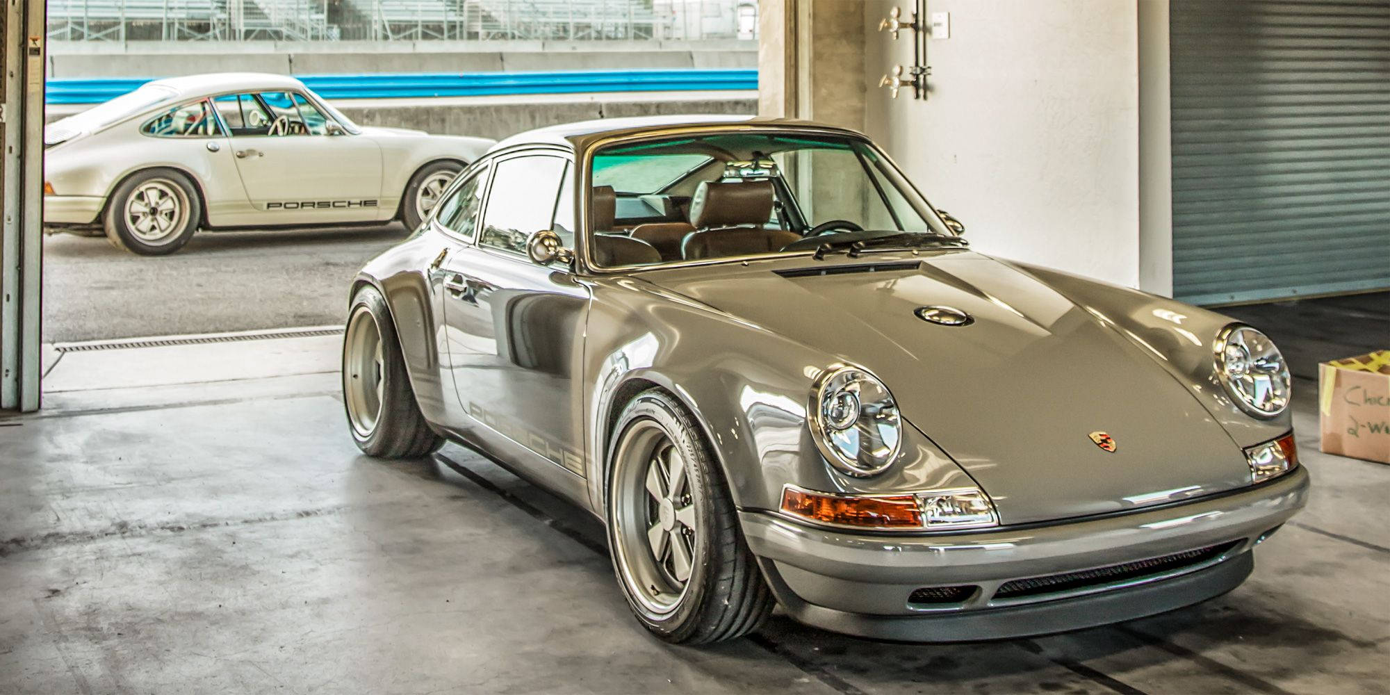 Singer保時捷911 Turbo車款 壁紙 — 一架時尚的銀色保時捷911配備寬輪胎停在車庫中，透過敞開的車門可以看到另一輛白色保時捷。