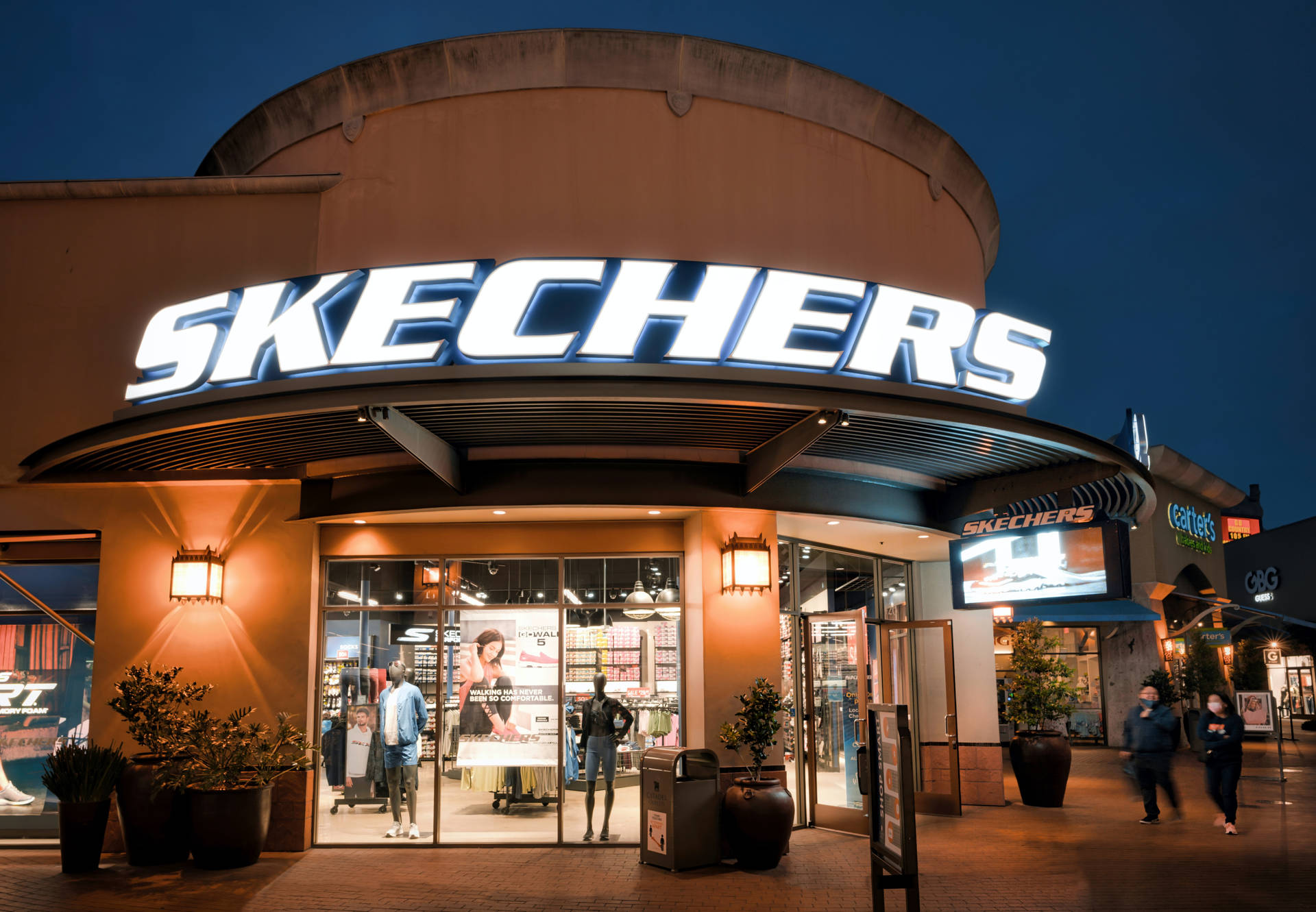 夜晚的Skechers零售店入口，帶有發光招牌和行人。