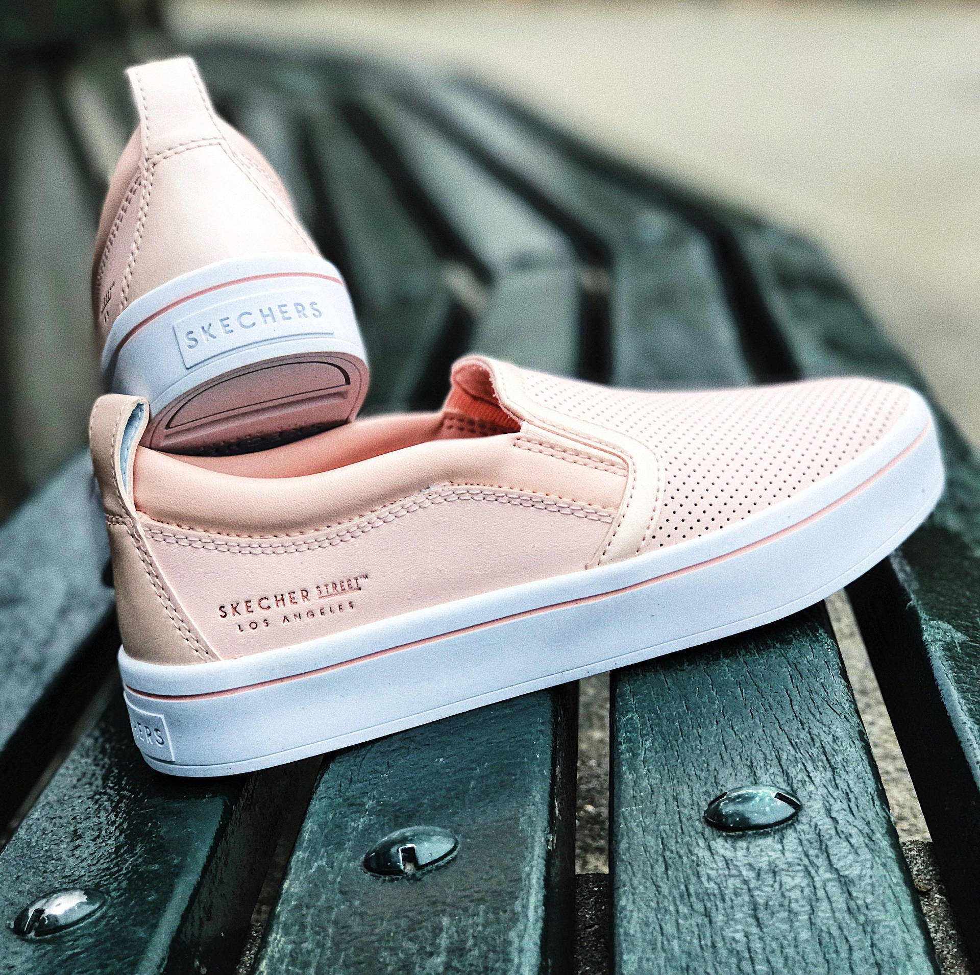 綠色木長椅上的淡粉紅色Skechers運動鞋。