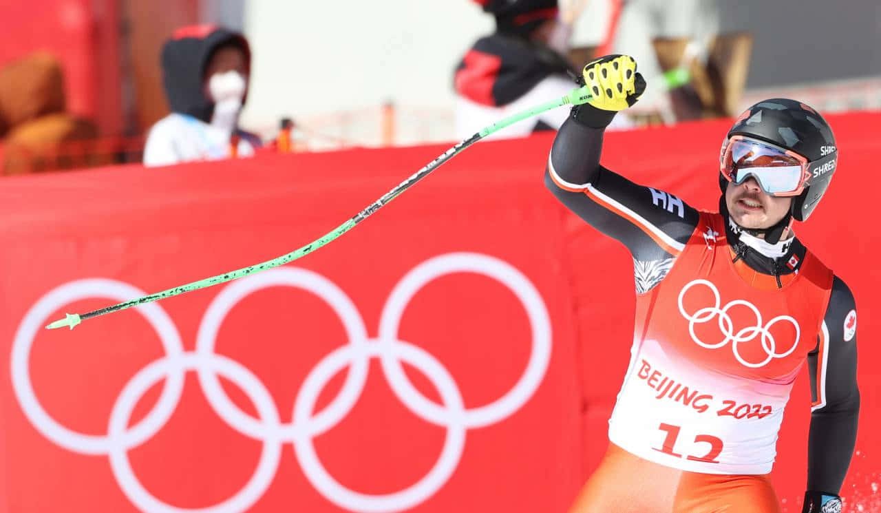  壁紙 — 一名滑雪跳躍運動員在北京2022年冬奧會上慶祝勝利，高舉一支滑雪杖，背景是紅色的奧運會背景。