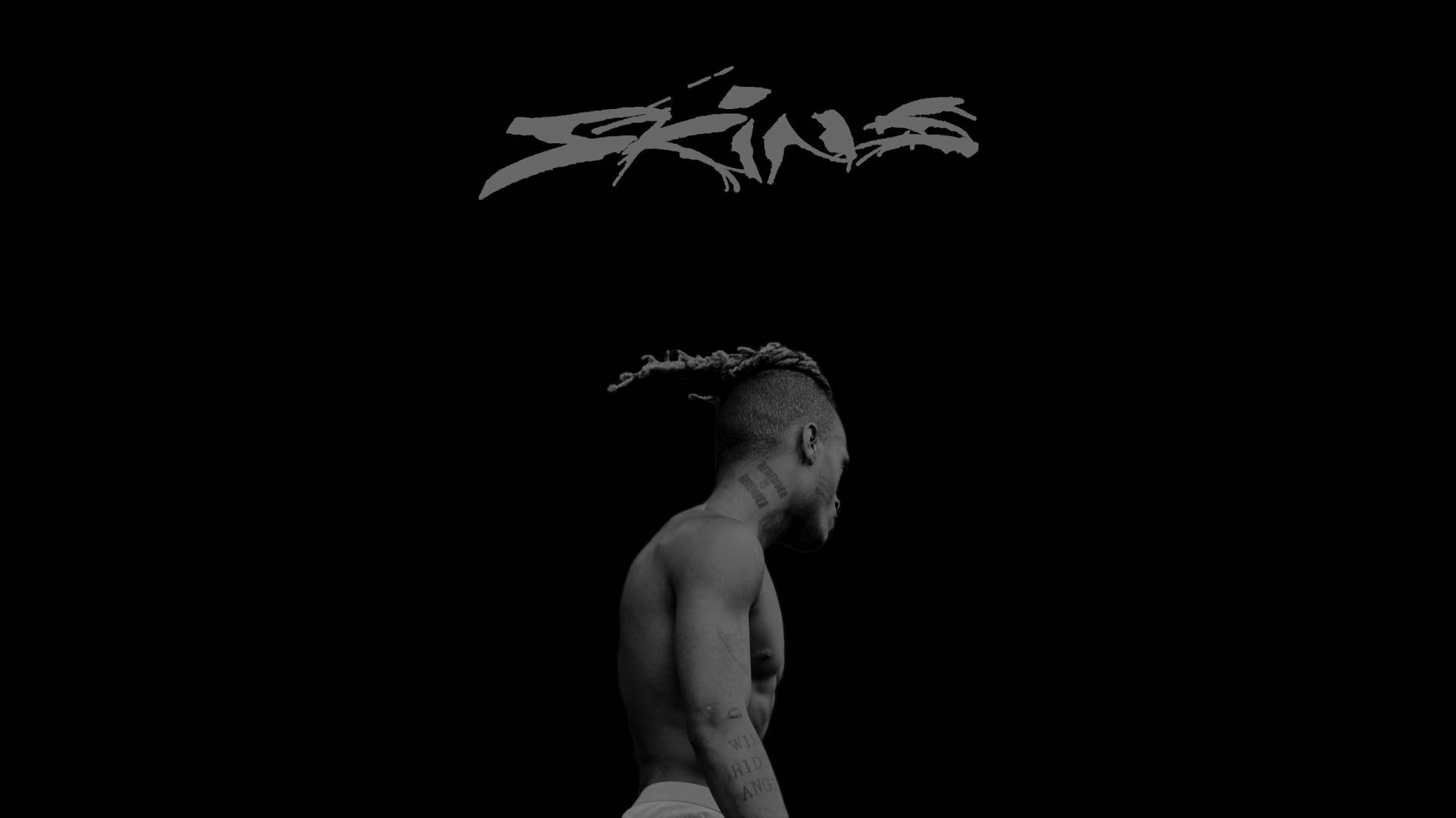 一個有紋身和辮子頭的男人，側面站在黑色背景前，帶有「Skins」文字。