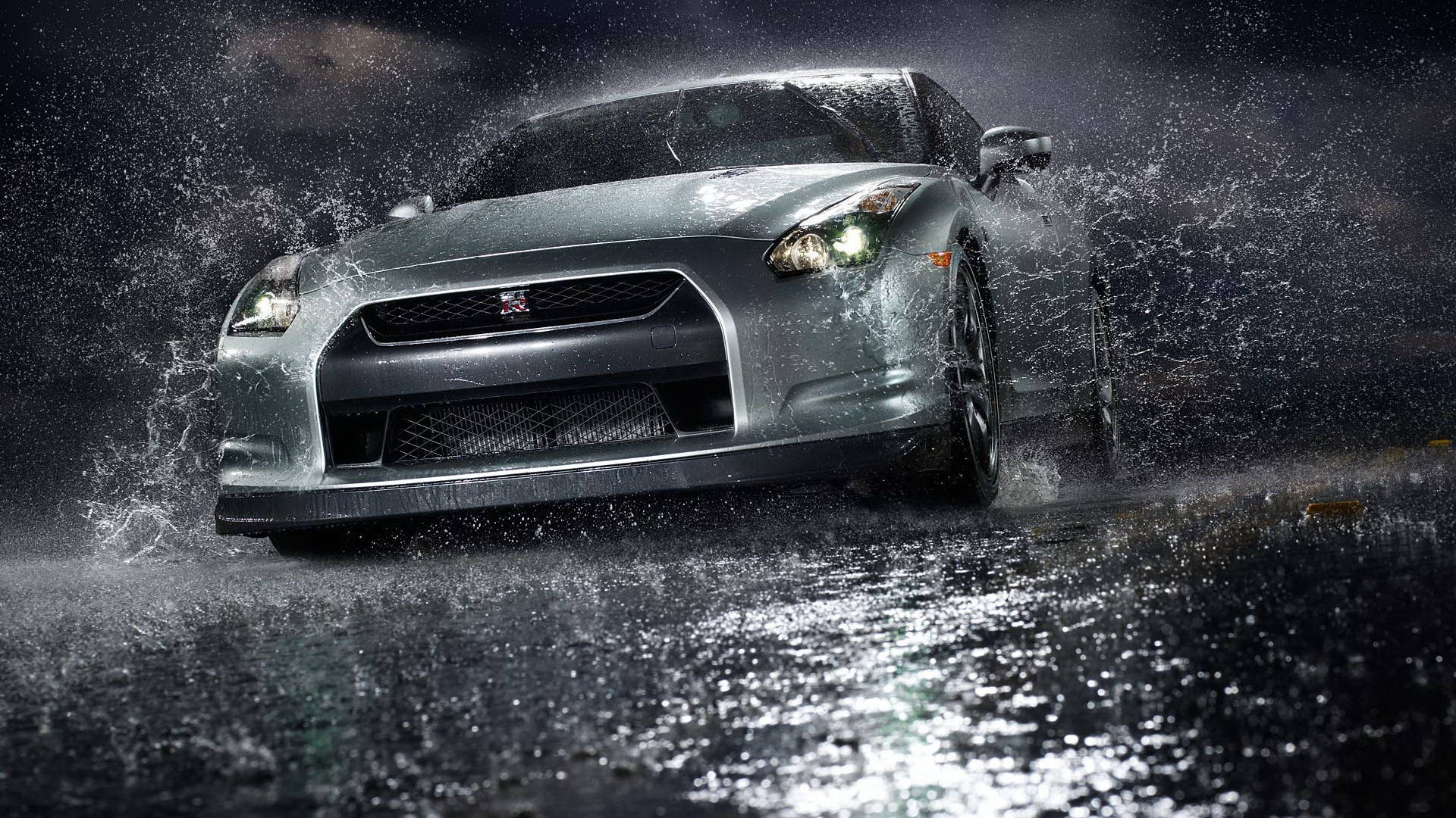 雨中閃耀的尼桑Skyline GTR R35 壁紙 — 一輛銀色跑車在暴雨中疾馳，在夜間濕漉漉的瀝青路上戲劇性地濺起水花。