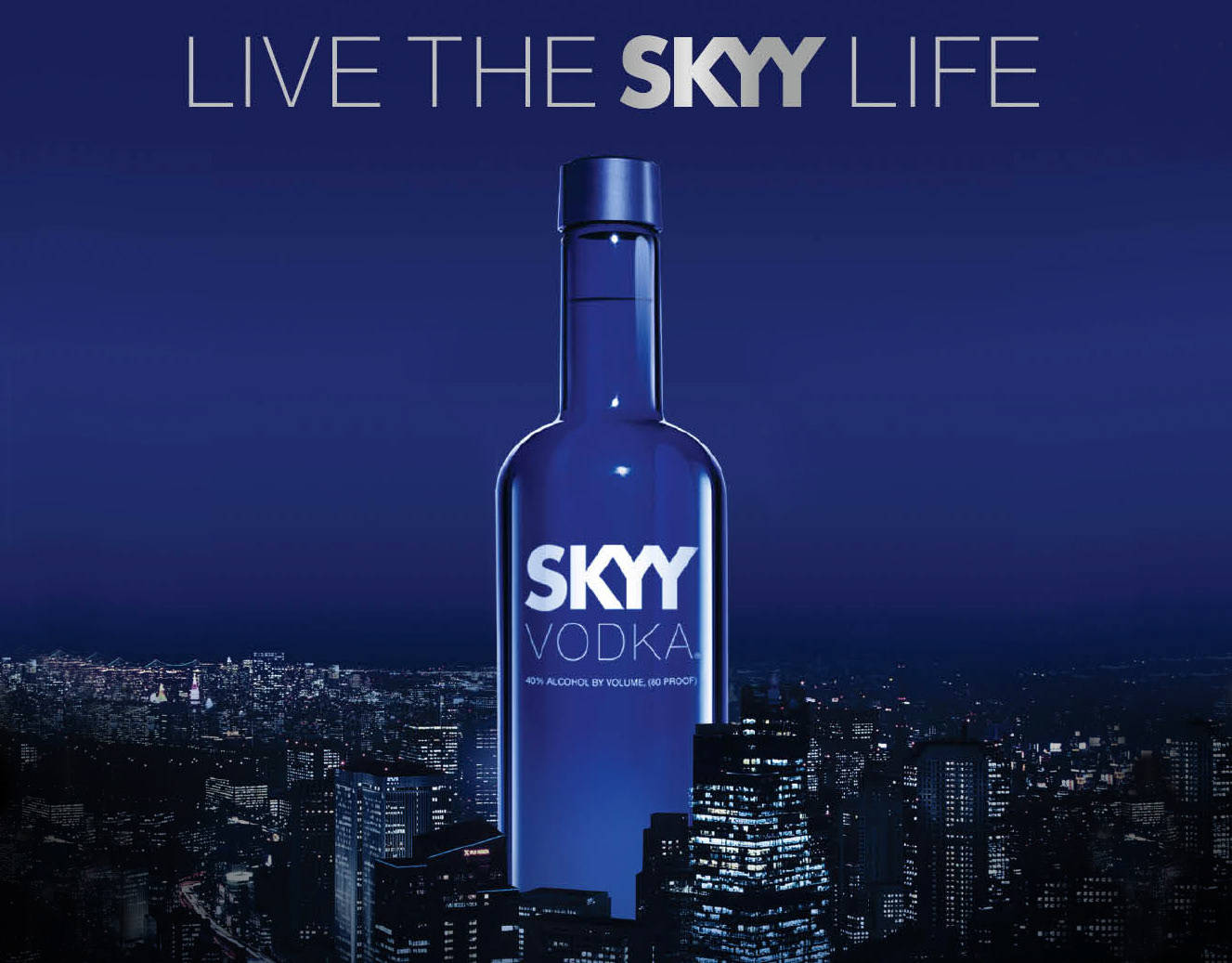 Skyy伏特加「活出Skyy人生」海報 壁紙 — 一個巨大的藍色Skyy伏特加酒瓶聳立在深藍色天空下閃閃發光的夜景城市景觀之上。
