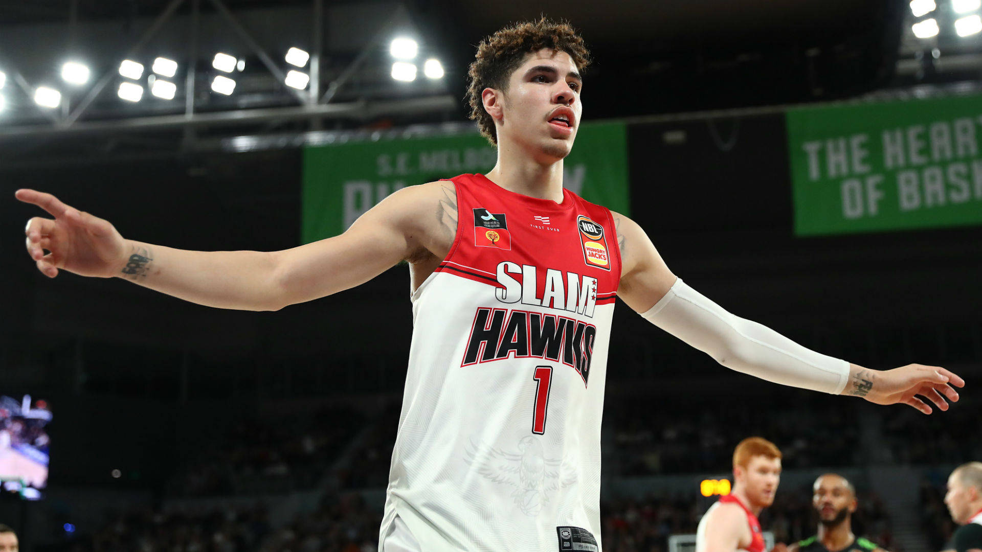 Slam Hawks 拉梅洛·鮑爾 壁紙 — 一名身穿白色和紅色 Slade Hawks 球衣、背號一的籃球運動員在明亮的場館燈光下強烈地做手勢。