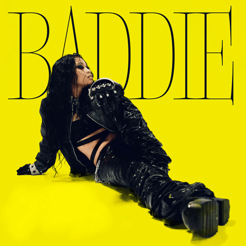 一位穿著黑色皮革的女性在明亮的黃色背景前擺姿勢，帶有「BADDIE」文字。