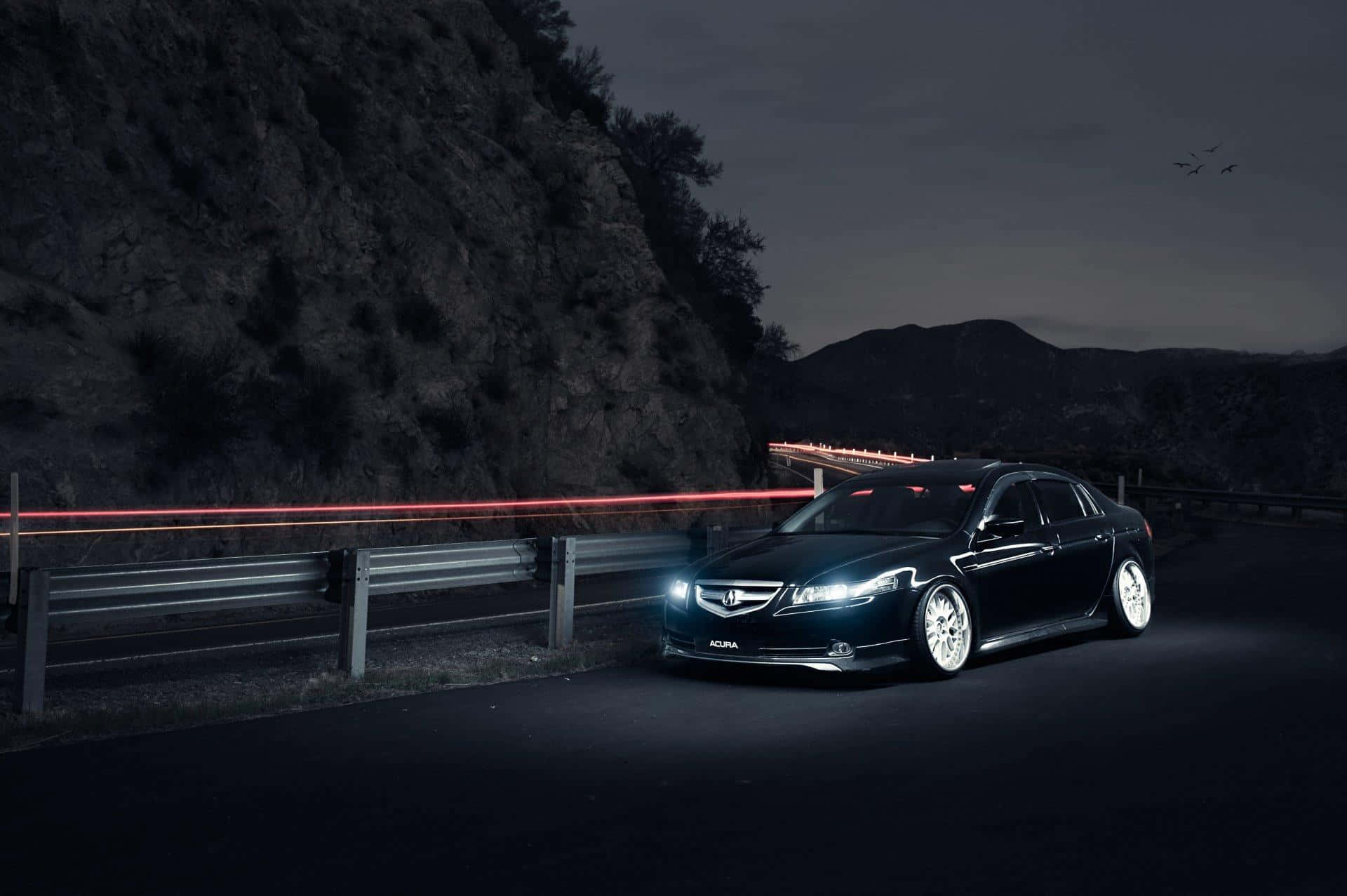 Acura Tl 桌布 壁紙 — 一輛時尚的黑色Acura轎車在暮色中蜿蜒的山路上，車頭燈下閃耀，遠方有山丘和飛鳥。