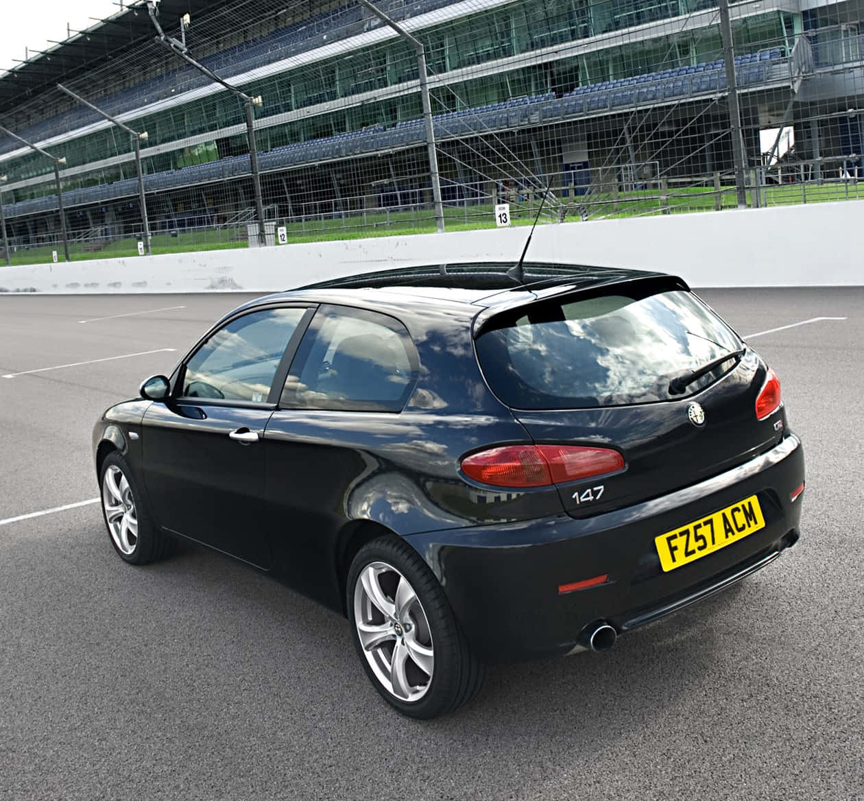 Alfa Romeo 147 桌布 壁紙 — 一架型格黑色愛快羅密歐147掀背車停在瀝青賽車場上，背景有看台。