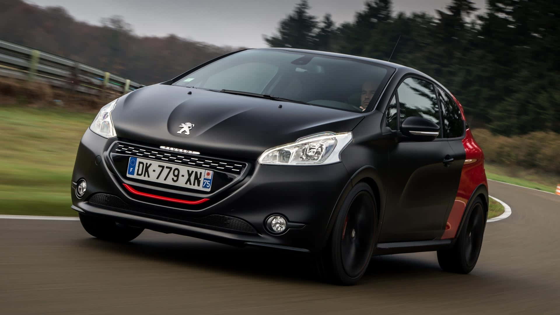 Peugeot 208 桌布 壁紙 — 一輛時尚的黑色和紅色標緻208跑車沿著蜿蜒的道路疾馳，背景是模糊的綠色植物和樹木。