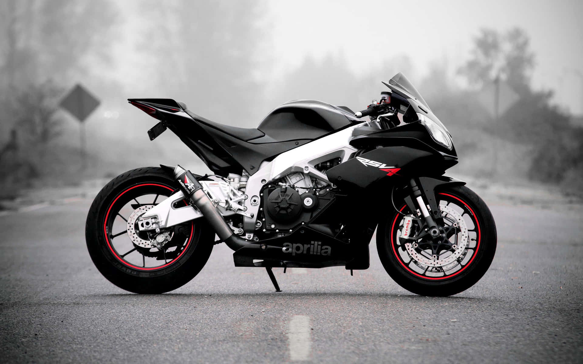  壁紙 — 一台時尚的黑白Aprilia RSV4電單車，帶有紅色點綴，停泊在霧氣瀰漫的道路上，其侵略性設計在柔和、霧濛濛的背景襯托下格外突出。