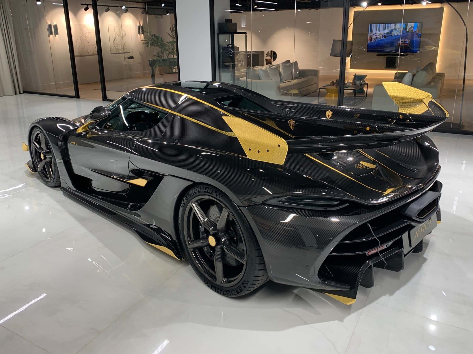  壁紙 — 一輛時尚的黑色和黃色 Koenigsegg 超級跑車，帶有碳纖維細節，展示在現代豪華展廳中，配有反光地板和玻璃牆。