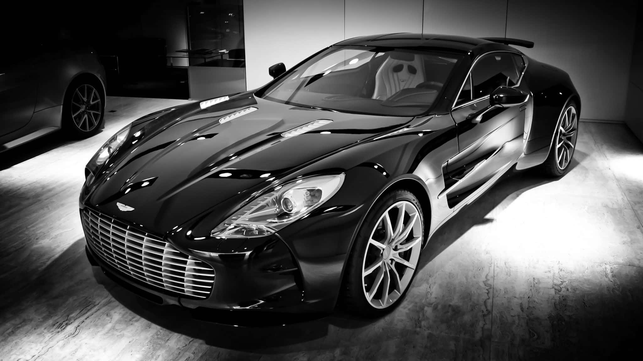 Aston Martin One-77 桌布 壁紙 — 一輛時尚的黑色Aston Martin跑車在簡約的陳列室中，在戲劇性的工作室燈光下閃閃發光。
