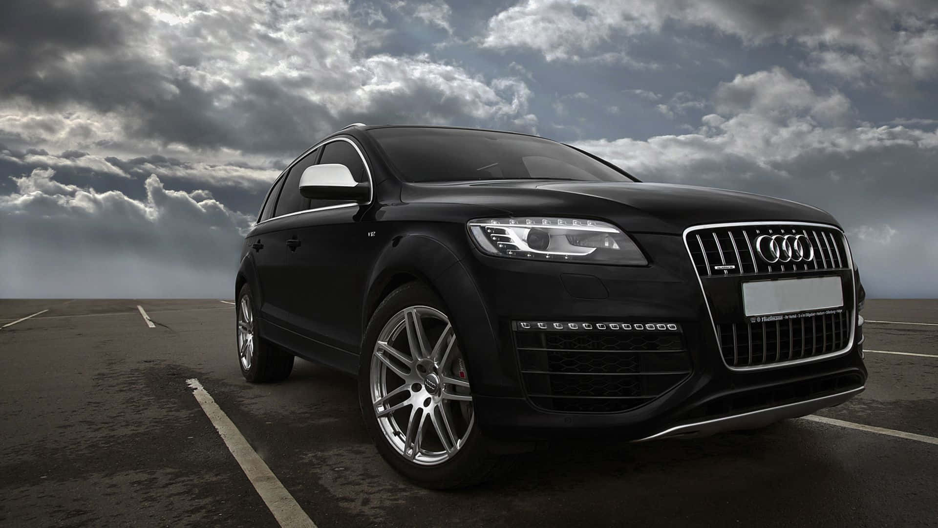 Audi Q7 桌布 壁紙 — 一輛時尚的黑色奧迪Q7 SUV停在空地上，天空烏雲密佈，氣氛戲劇化。