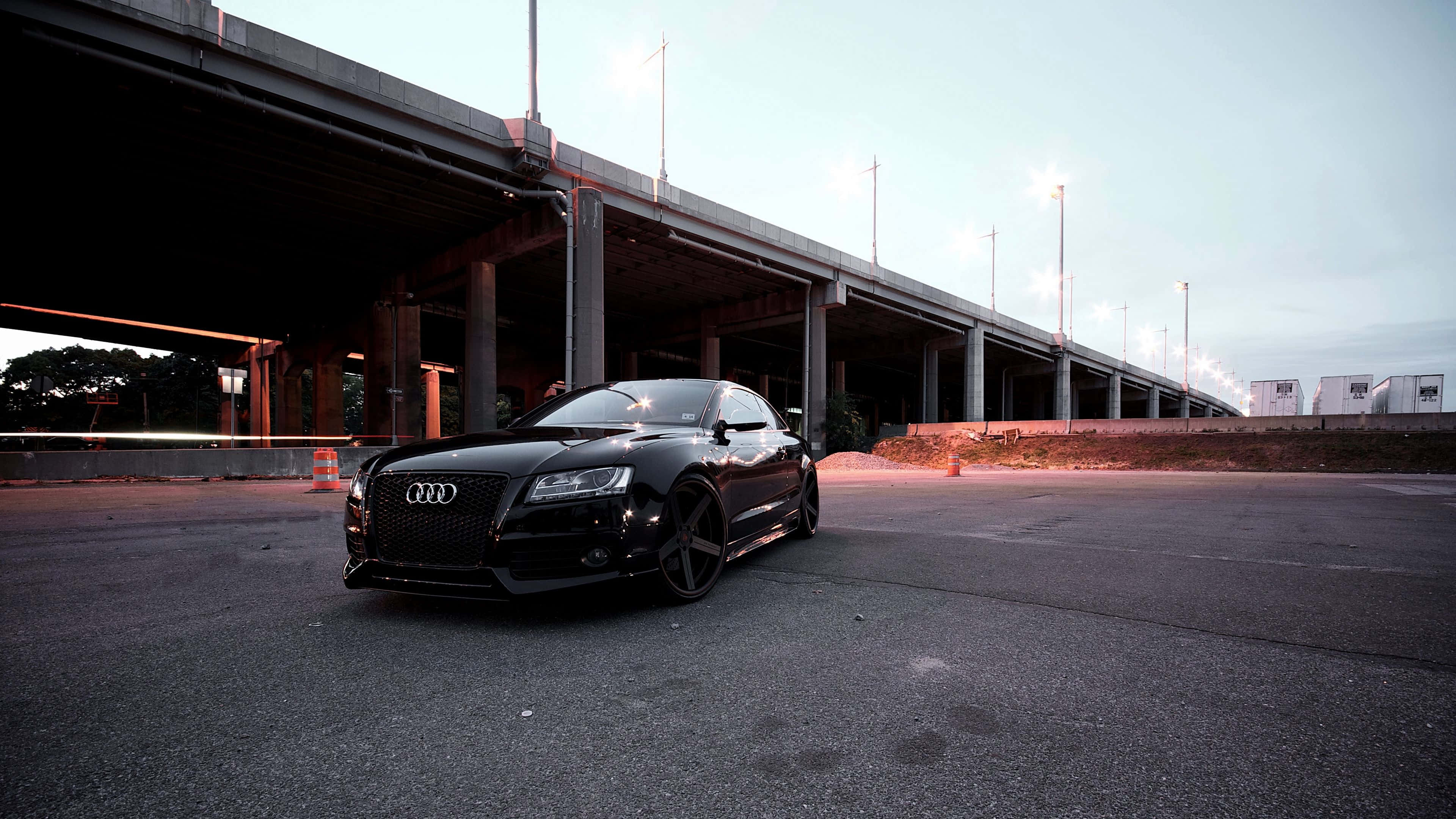 Audi A4 桌布 壁紙 — 一輛時尚的黑色奧迪跑車停泊在混凝土天橋下，暮色中街燈閃爍。
