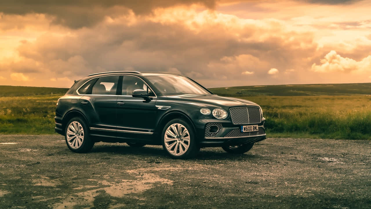 Bentley Bentayga 桌布 壁紙 — 一架時尚黑色賓利Bentayga SUV停泊在碎石路上，背景是戲劇性的金色日落天空。