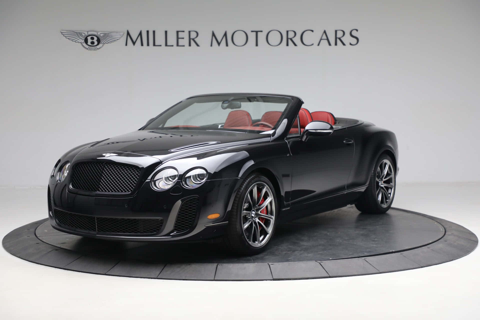 Bentley Continental Supersports 桌布 壁紙 — 一輛時尚的黑色賓利敞篷車，配備紅色皮革座椅，在工作室環境中的圓形平台上展示。