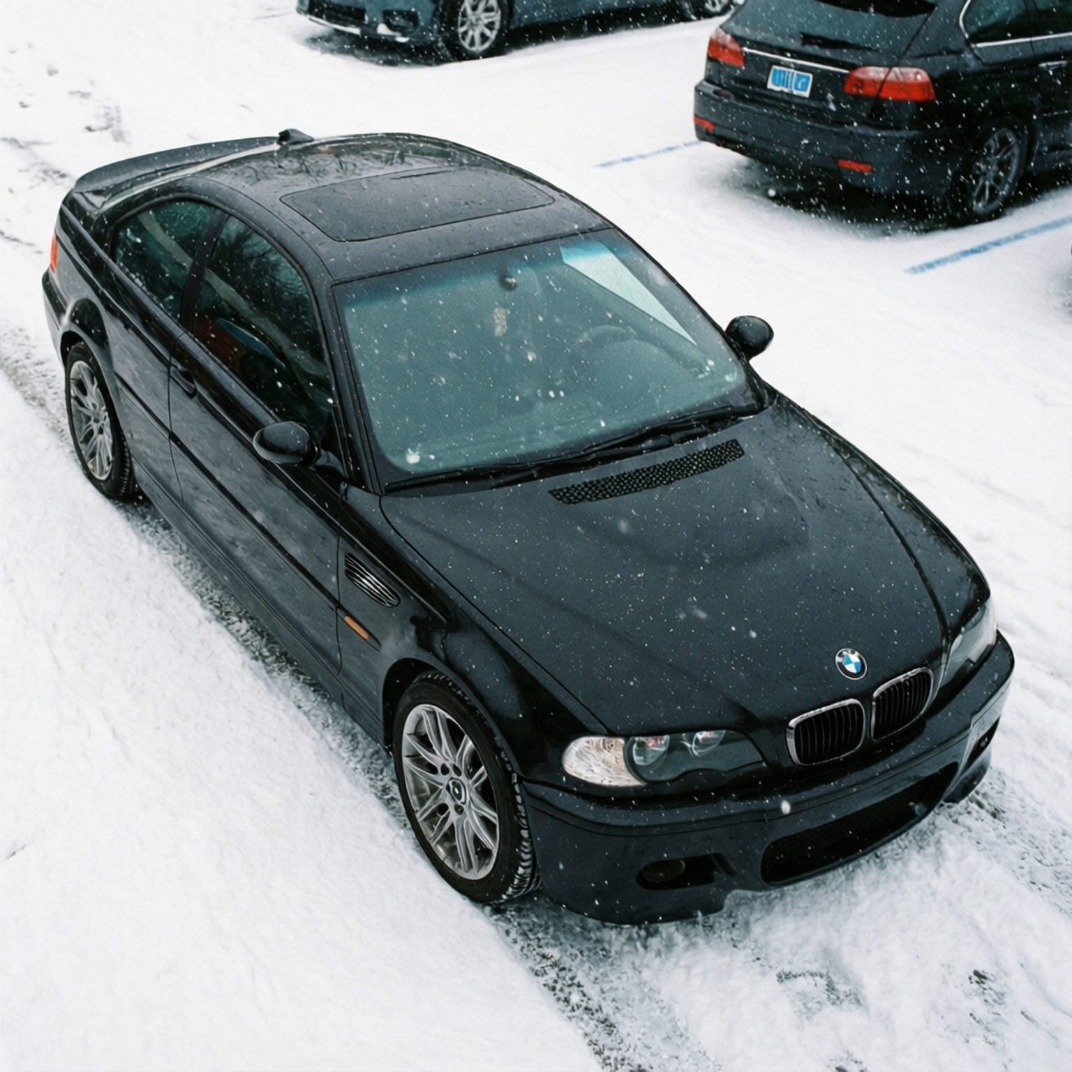 黑色寶馬轎跑車在下雪時停泊在積雪的停車場。