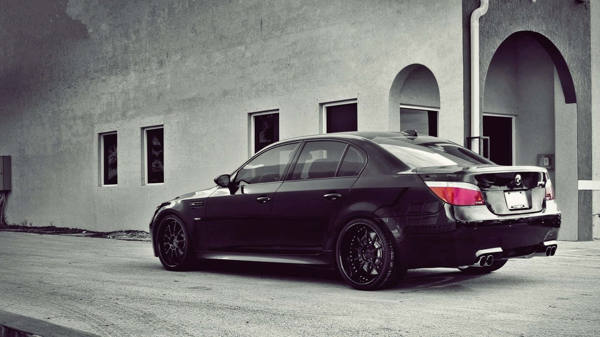 Bmw M5 桌布 壁紙 — 一架型格黑色BMW房車配備訂製輪圈，停泊在極簡混凝土建築前，建築帶有拱形窗戶。