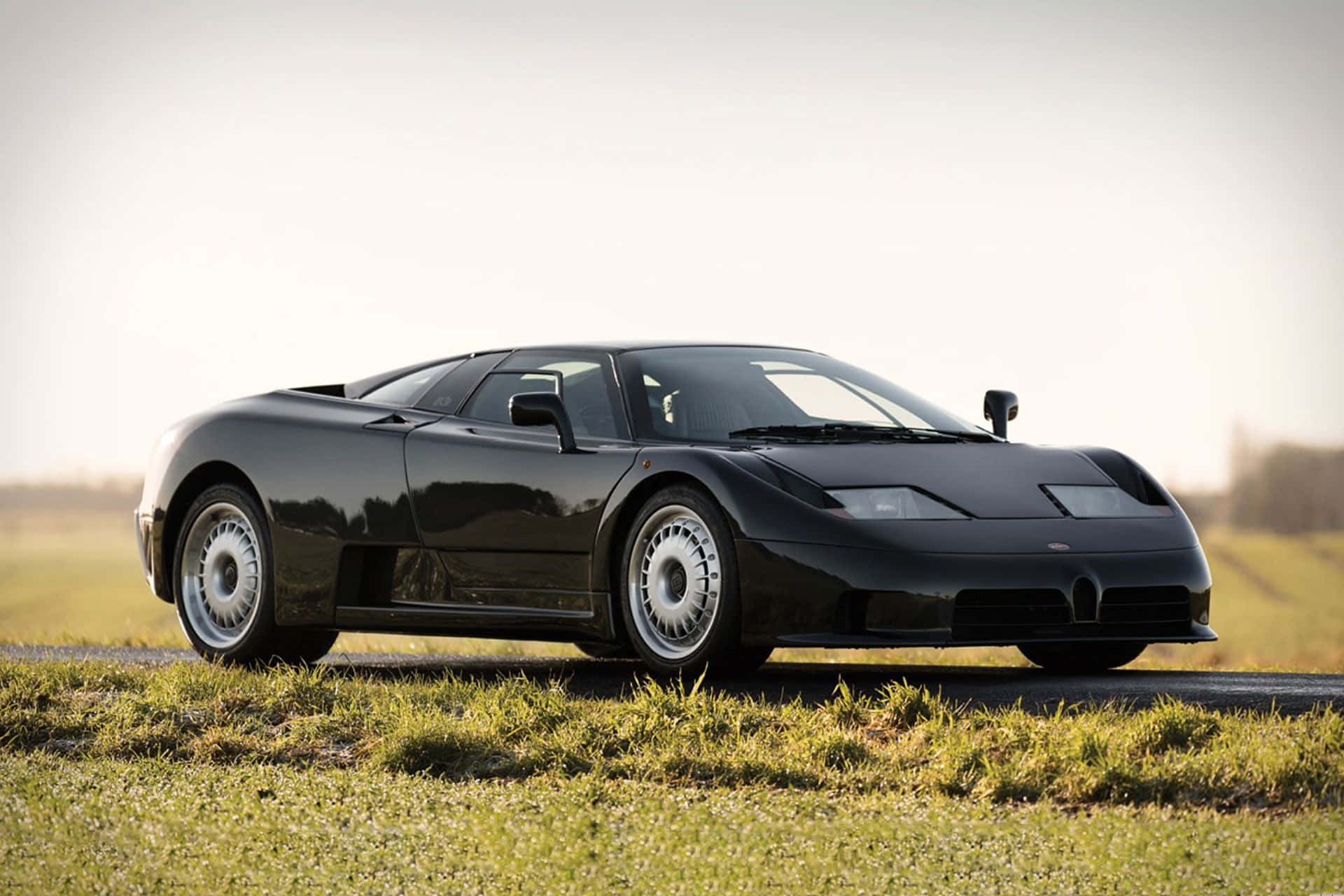 Bugatti Eb110 桌布 壁紙 — 一架流線型黑色Bugatti EB110超級跑車在柔和的金色時光下停泊在草地路邊。