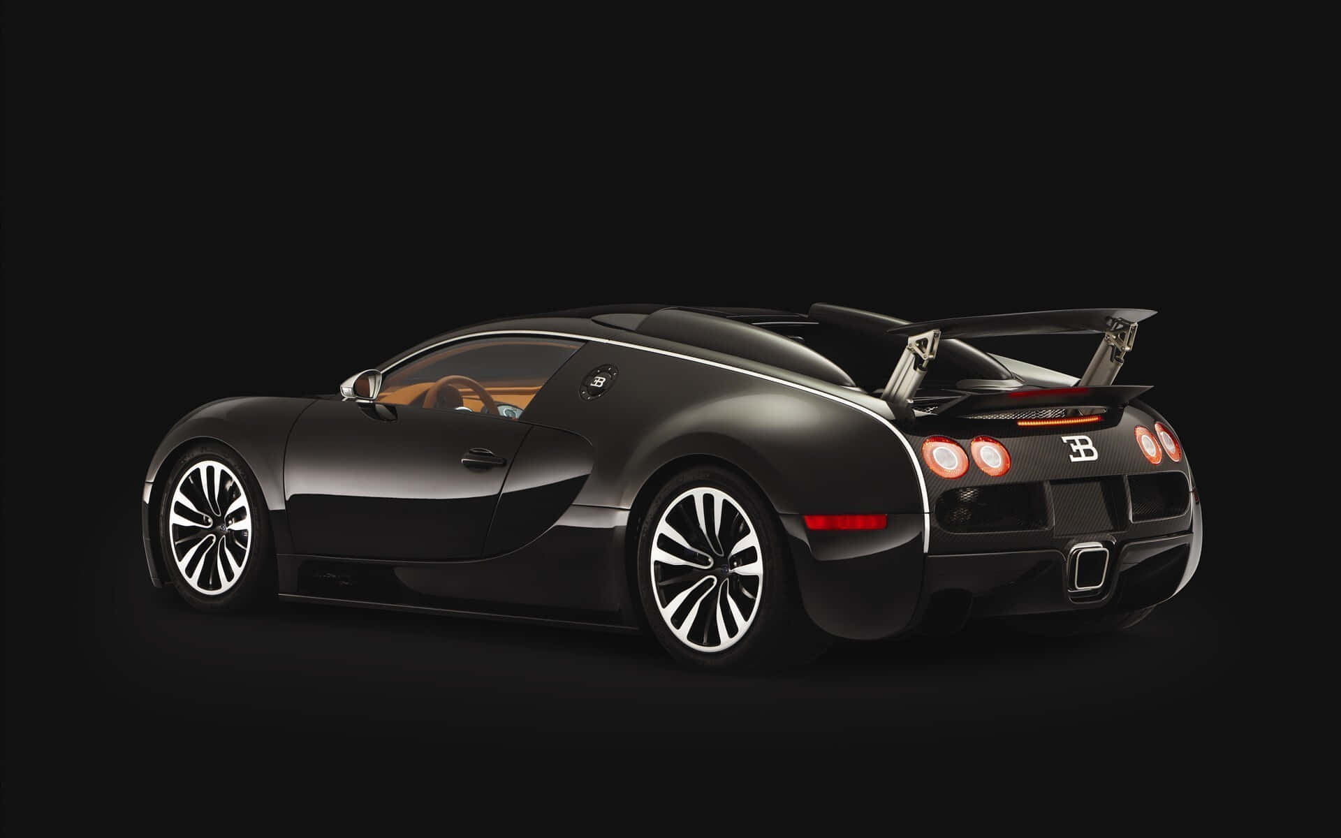 Bugatti Veyron 桌布 壁紙 — 一架時尚的黑色Bugatti Veyron跑車，帶有突出的後翼和發光的尾燈，矗立在純黑色背景上。