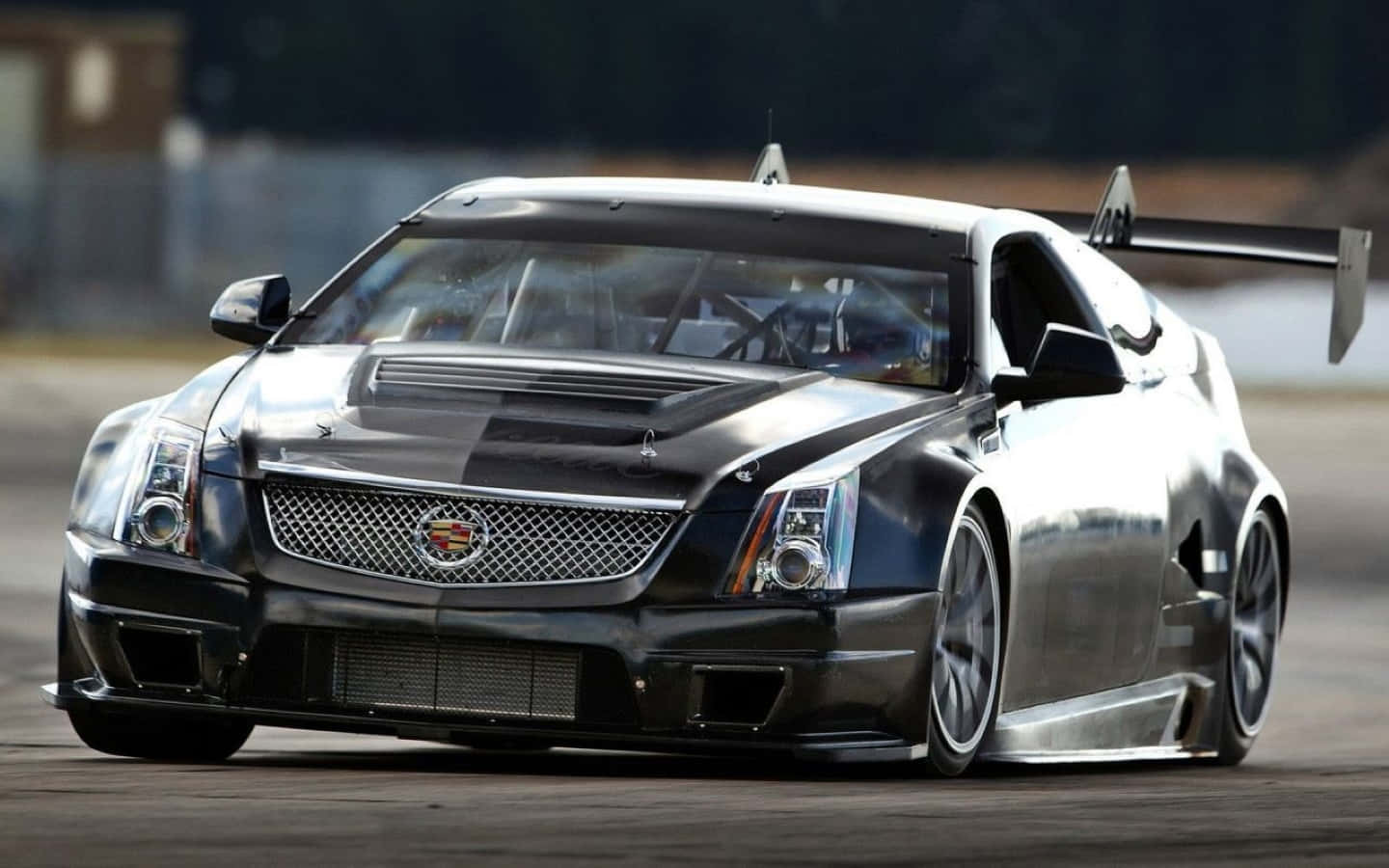 Cadillac Cts 桌布 壁紙 — 一輛時尚的黑色凱迪拉克賽車，帶有大型後尾翼，在明亮的日光下在賽道上飛馳。