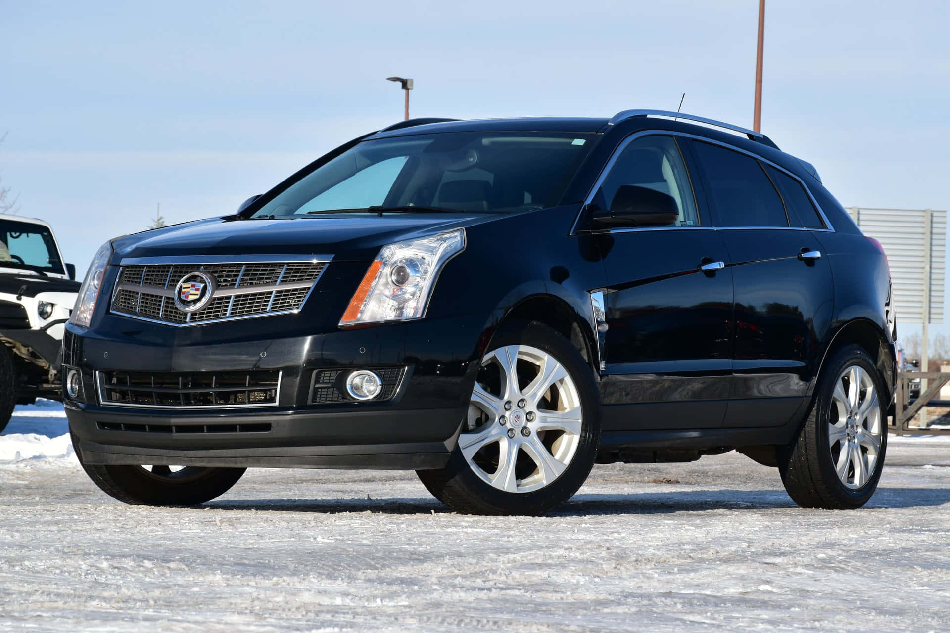 Cadillac Srx 桌布 壁紙 — 一輛時尚的黑色Cadillac SRX SUV停泊在雪地上，天空清澈湛藍，陽光在其拋光表面反射。