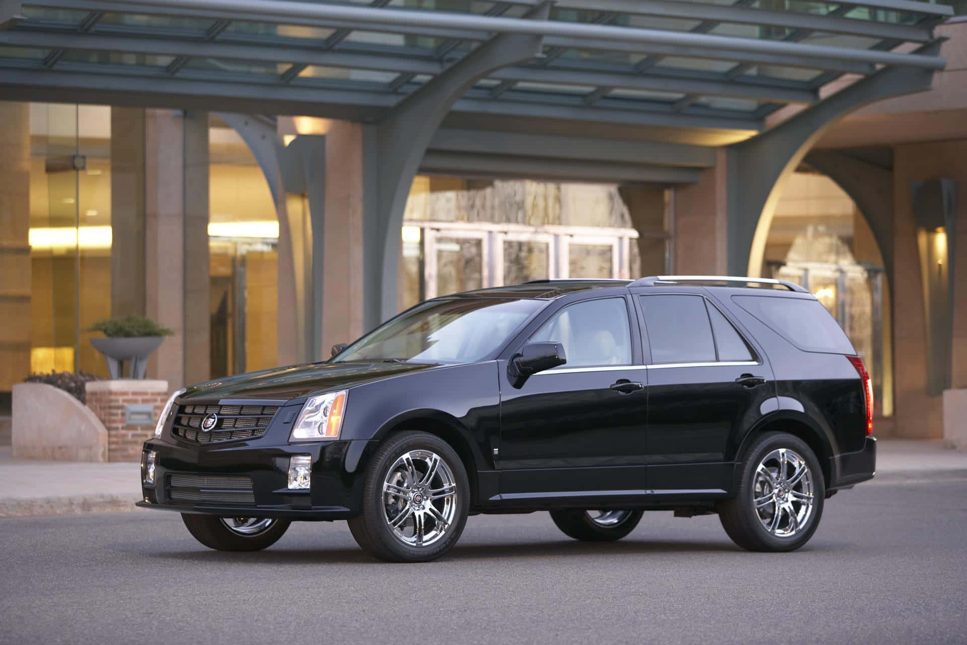 Cadillac Srx 桌布 壁紙 — 一輛時尚的黑色凱迪拉克SUV停在一棟現代玻璃和石材建築前。