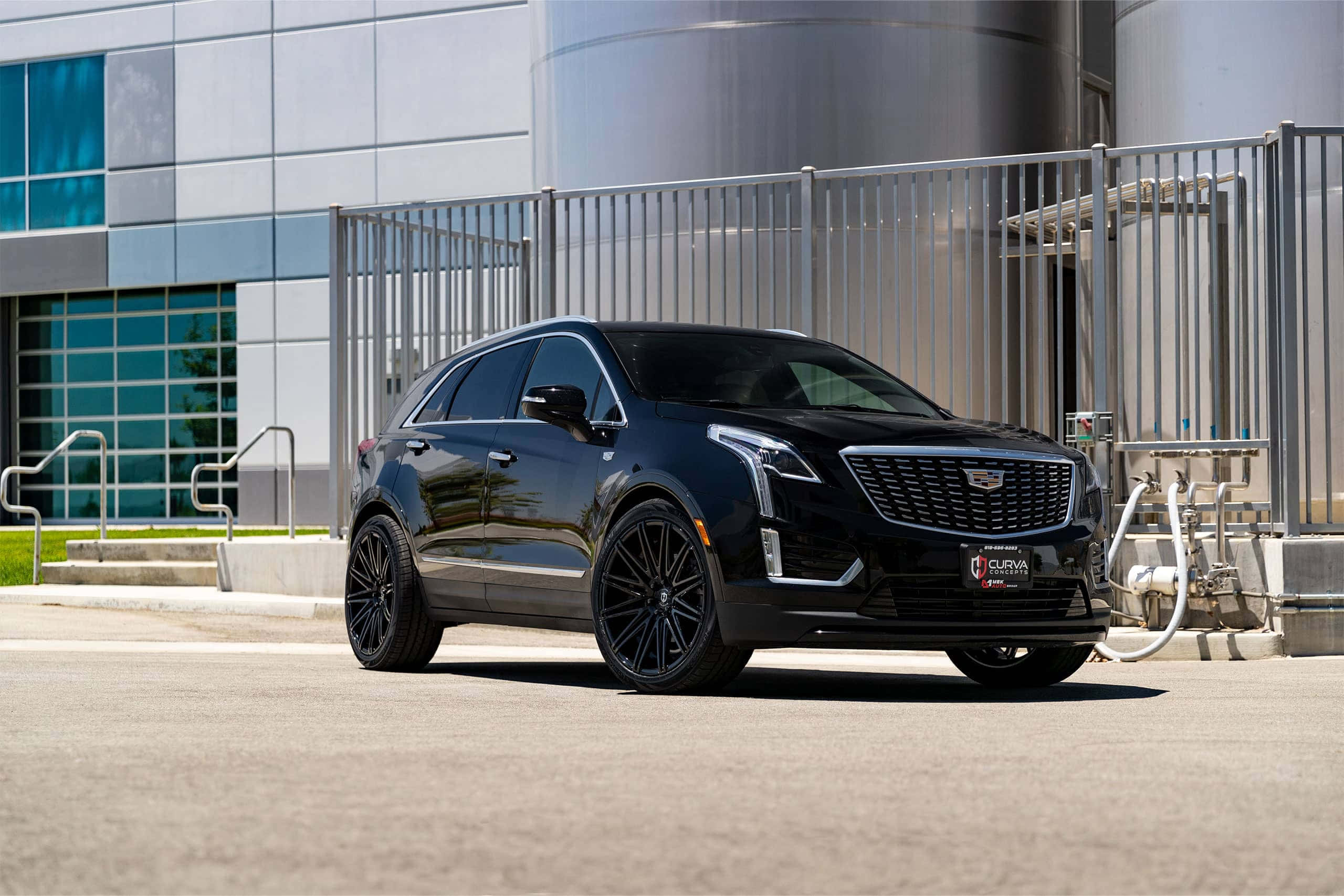 Cadillac Xt5 桌布 壁紙 — 一輛時尚的黑色凱迪拉克SUV停在一棟現代工業建築前，建築帶有金屬圍欄和大型銀色儲罐。