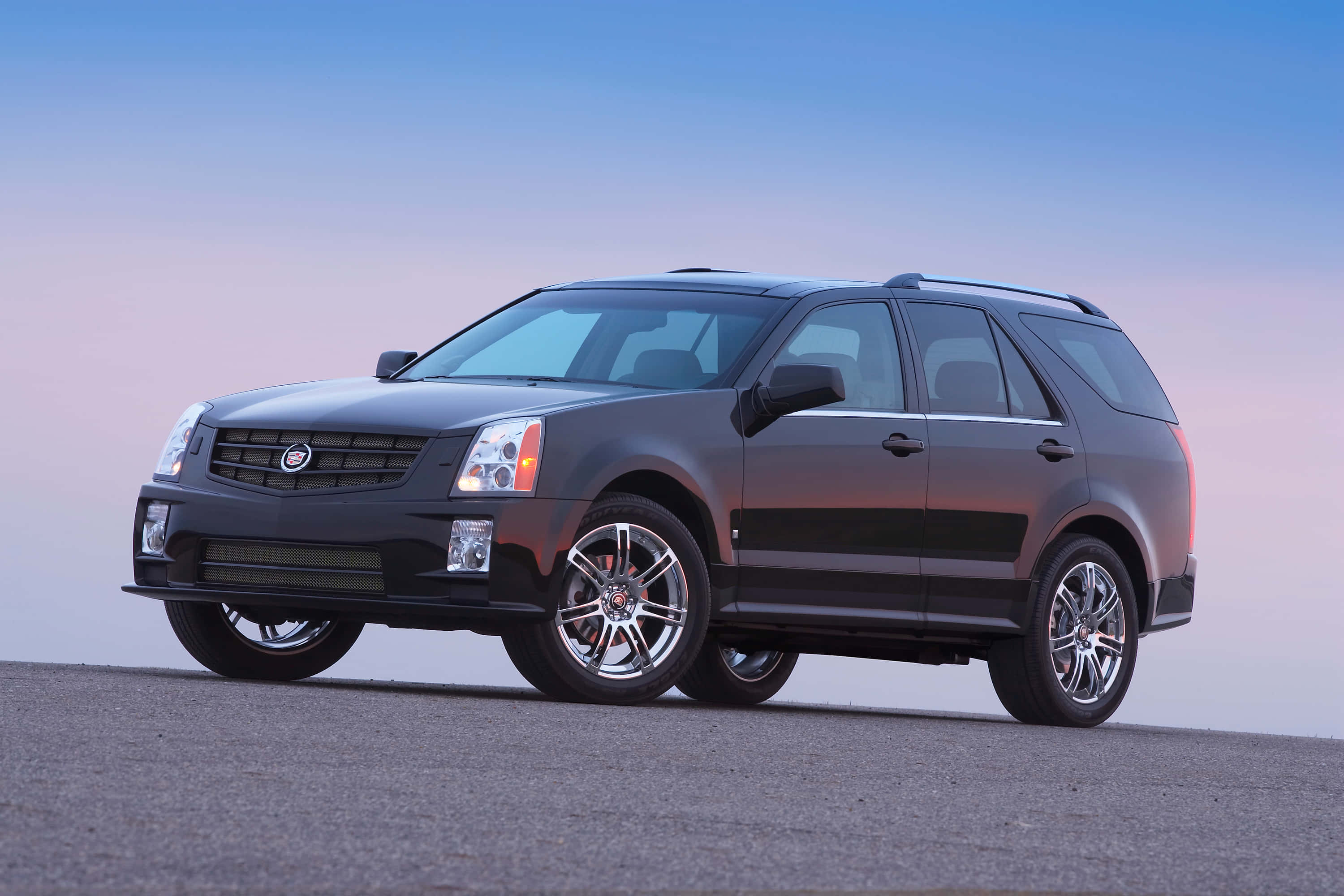Cadillac Srx 桌布 壁紙 — 一輛時尚的黑色Cadillac SUV停在瀝青路上，背景是柔和暮色天空，帶有漸變藍色和粉紅色調。