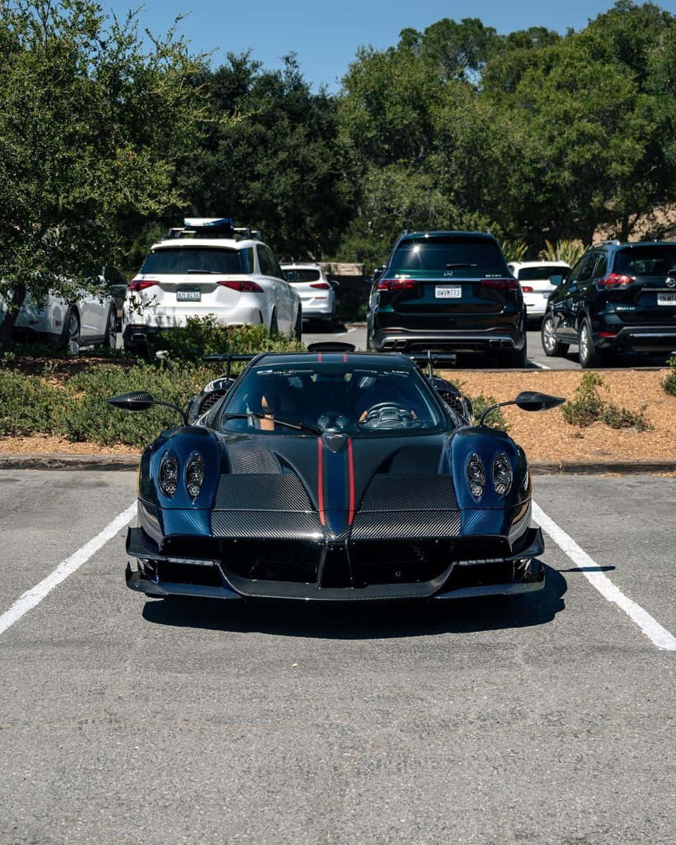 Pagani Huayra Roadster Bc 桌布 壁紙 — 一輛時尚的黑色碳纖維超級跑車，帶有紅色點綴，停在陽光明媚的停車場，周圍有樹木和其他車輛。
