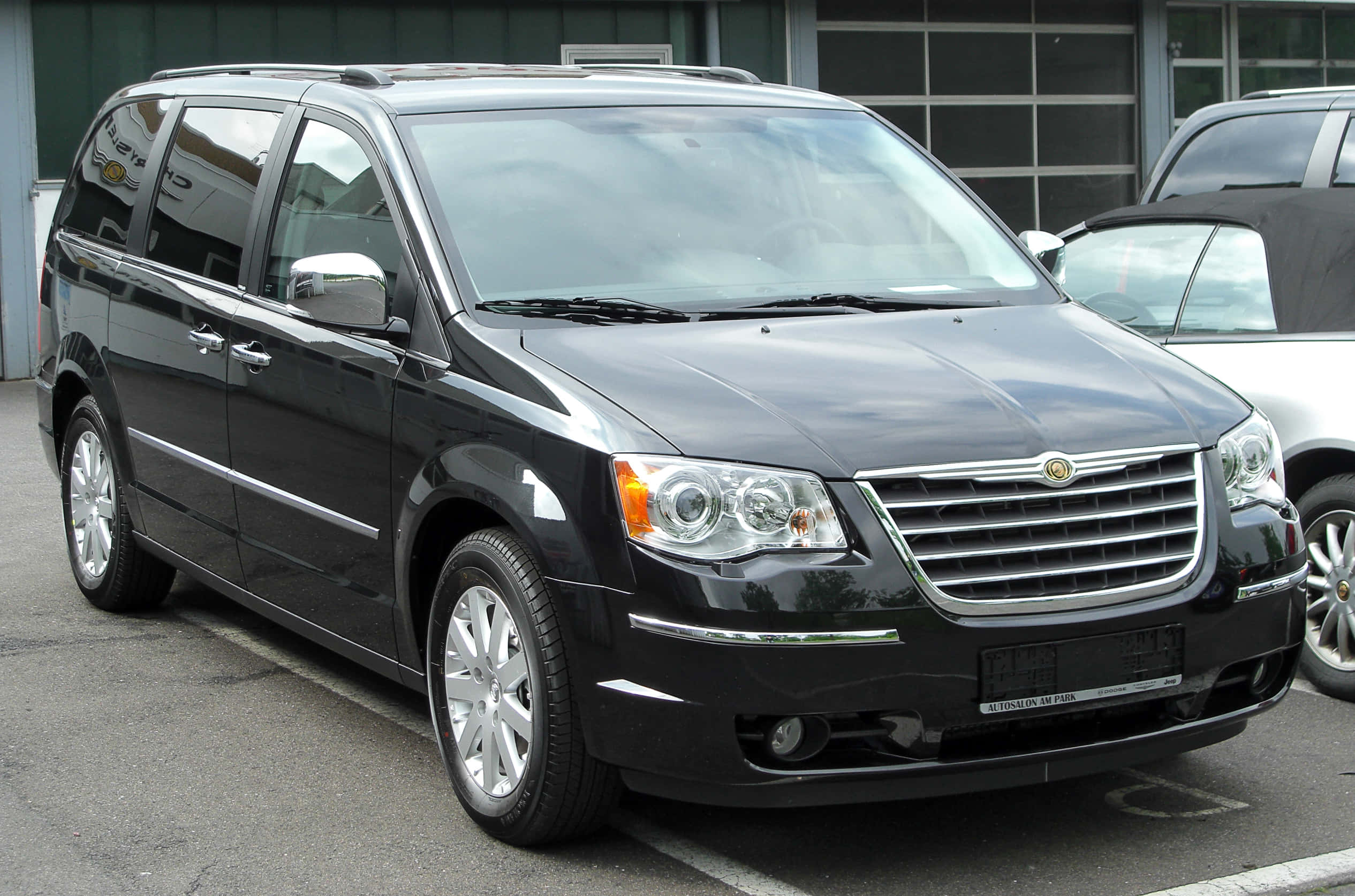Chrysler Voyager 桌布 壁紙 — 一架時尚的黑色克萊斯勒Town and Country小型貨車停泊在停車場，背景有現代建築。