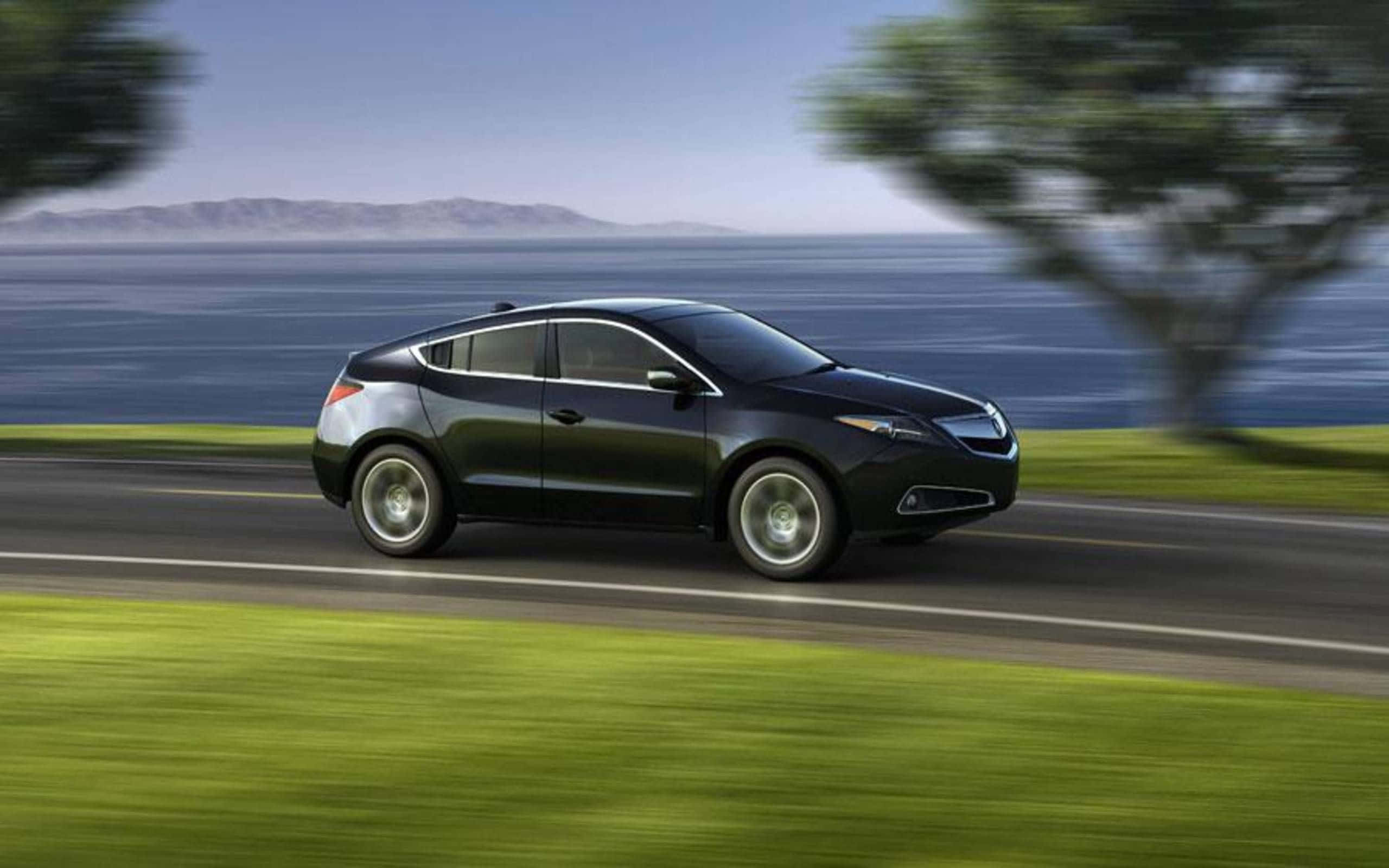 Acura Zdx 桌布 壁紙 — 一輛時尚黑色轎跑車沿著海岸公路飛馳，背景是模糊的綠植和遠處的山脈，天空晴朗。