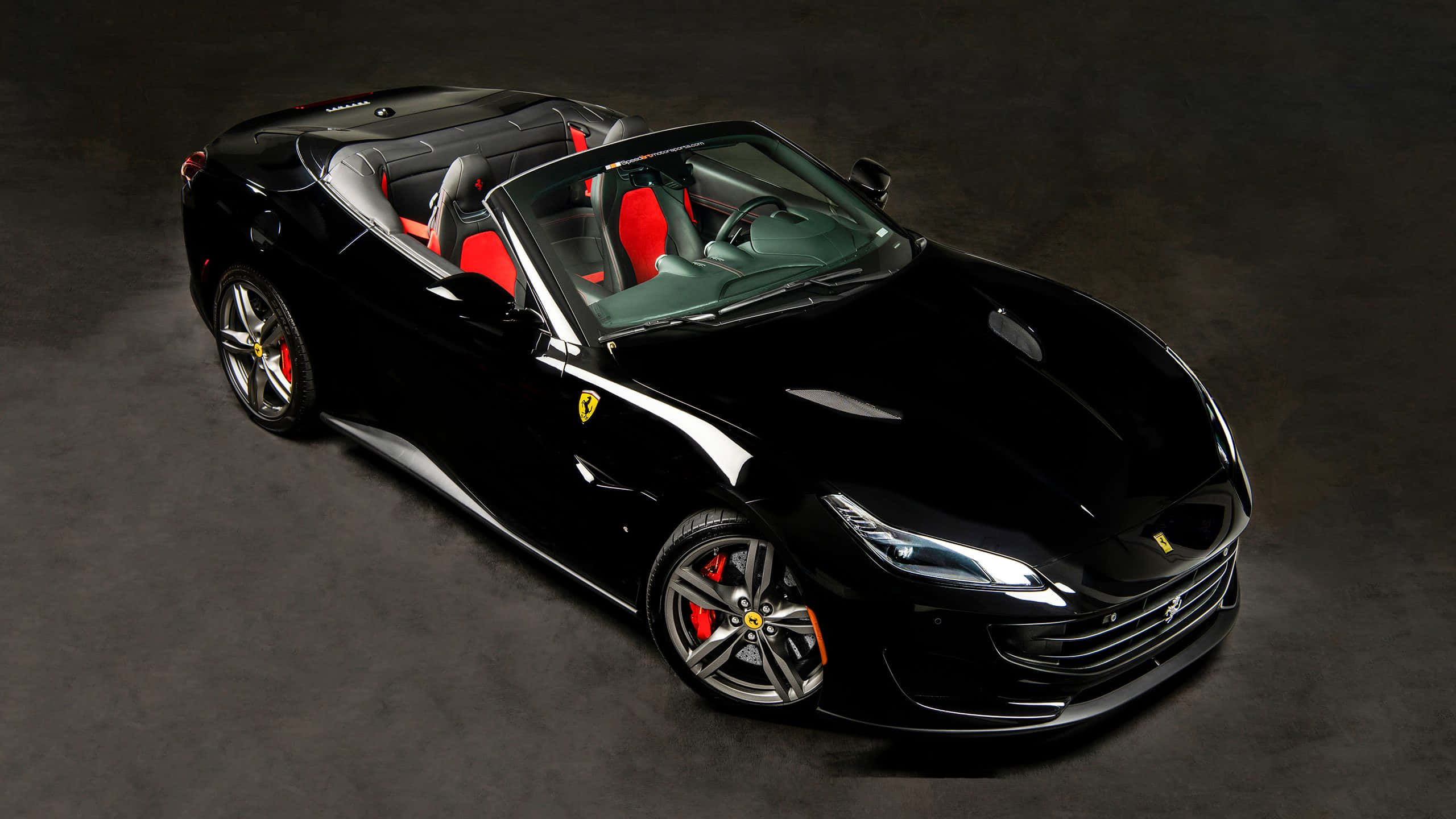 Ferrari Portofino 桌布 壁紙 — 一輛時尚的黑色法拉利開篷車，配備紅色座椅和銀色輪圈，在深灰色背景下的攝影棚燈光中閃閃發光。