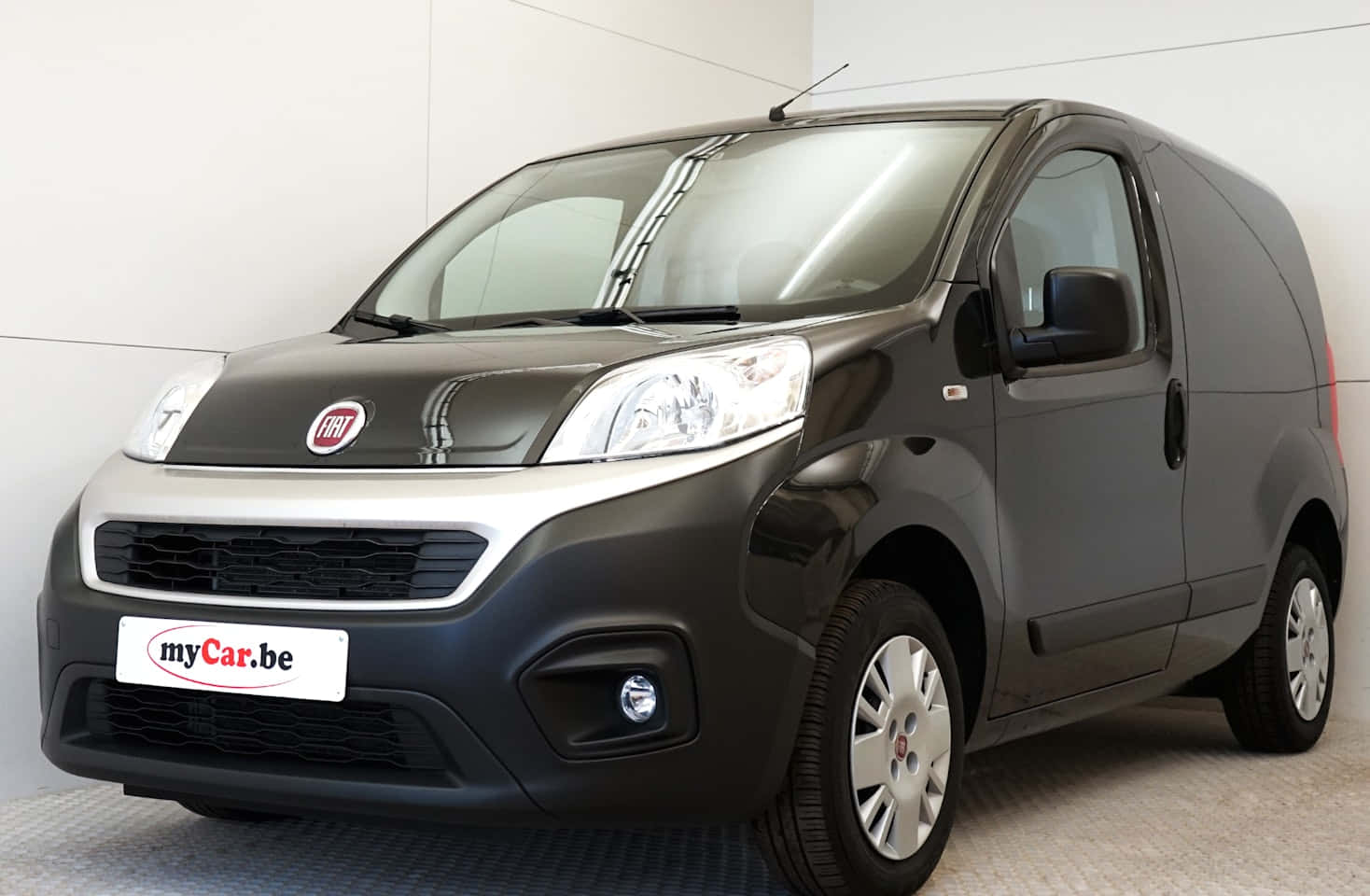 Fiat Fiorino 桌布 壁紙 — 一架時尚黑色Fiat客貨車帶有銀色飾邊，停放在室內灰色地板上，背景是純白色牆壁。