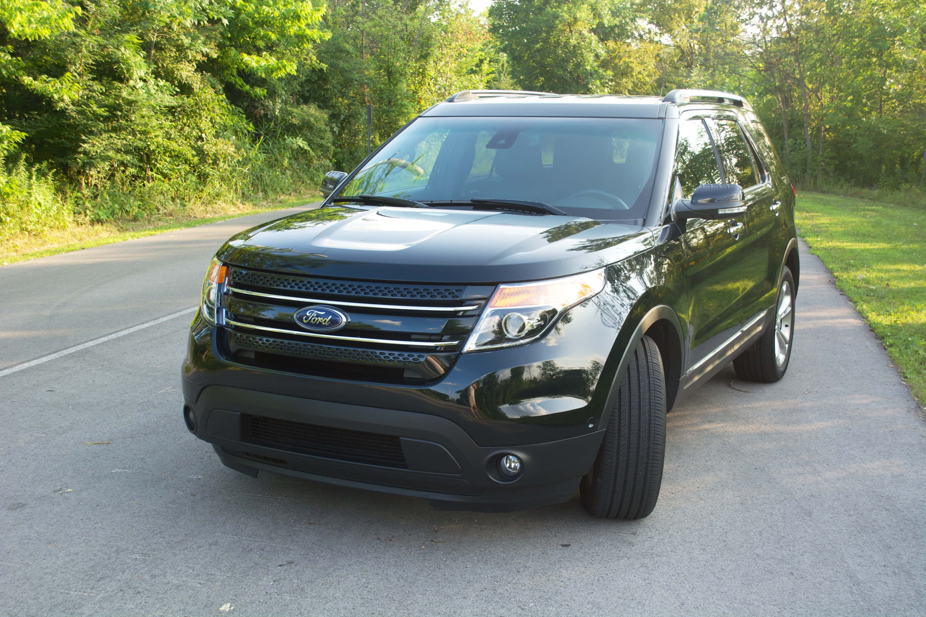 Ford Explorer 桌布 壁紙 — 一輛時尚的黑色福特Explorer SUV停泊在寧靜的瀝青路上，兩旁綠樹成蔭，草地茂盛。
