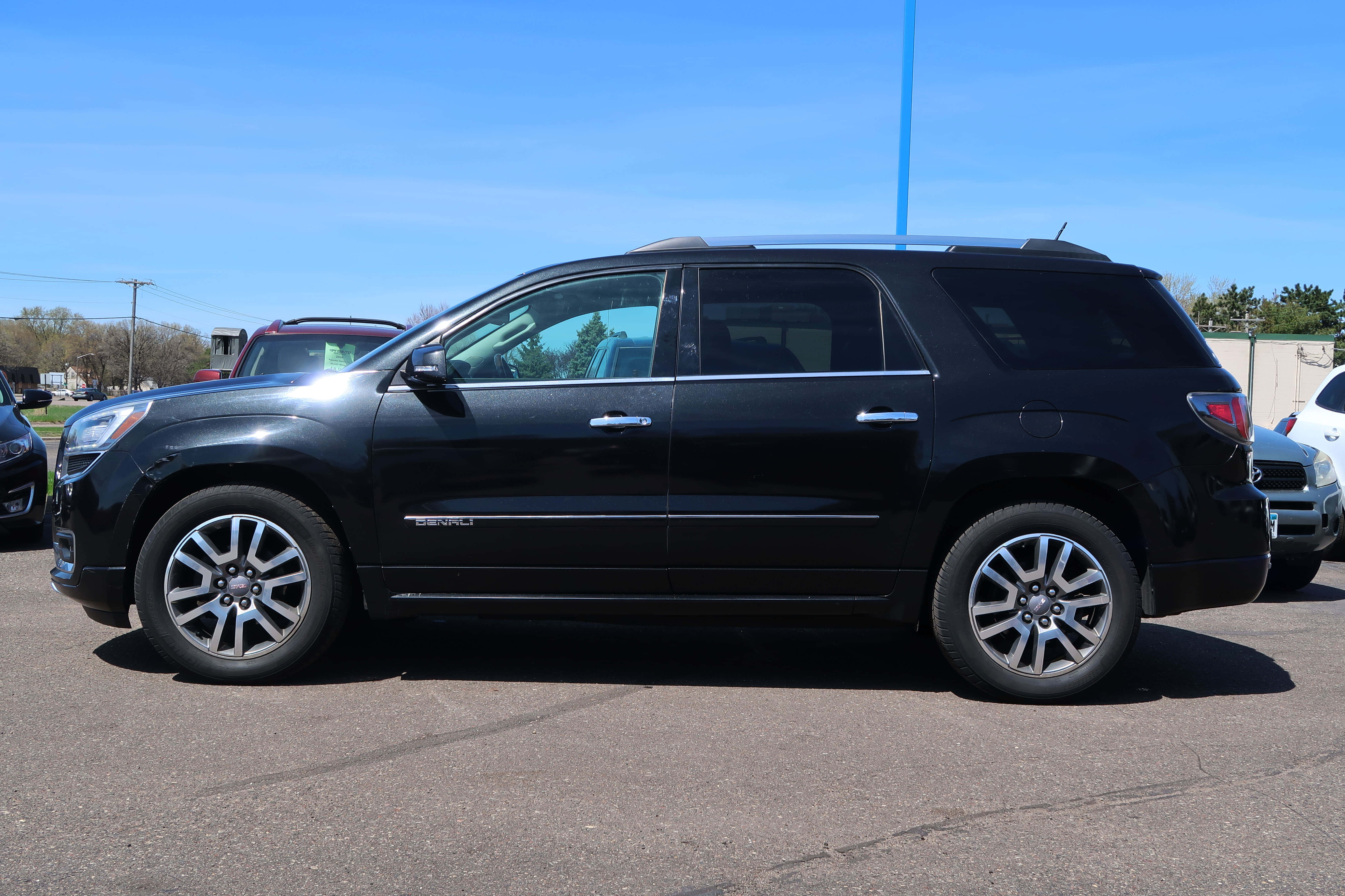 Gmc Acadia 桌布 壁紙 — 一輛時尚的黑色GMC Acadia SUV停泊在陽光明媚的停車場，天空清澈湛藍，附近有其他車輛。