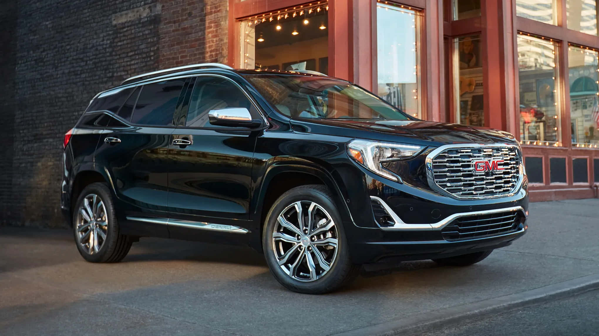 Gmc Terrain 桌布 壁紙 — 一輛時尚的黑色GMC Acadia SUV停泊在城市的街道上，旁邊是一棟帶有溫暖窗燈的磚砌建築。