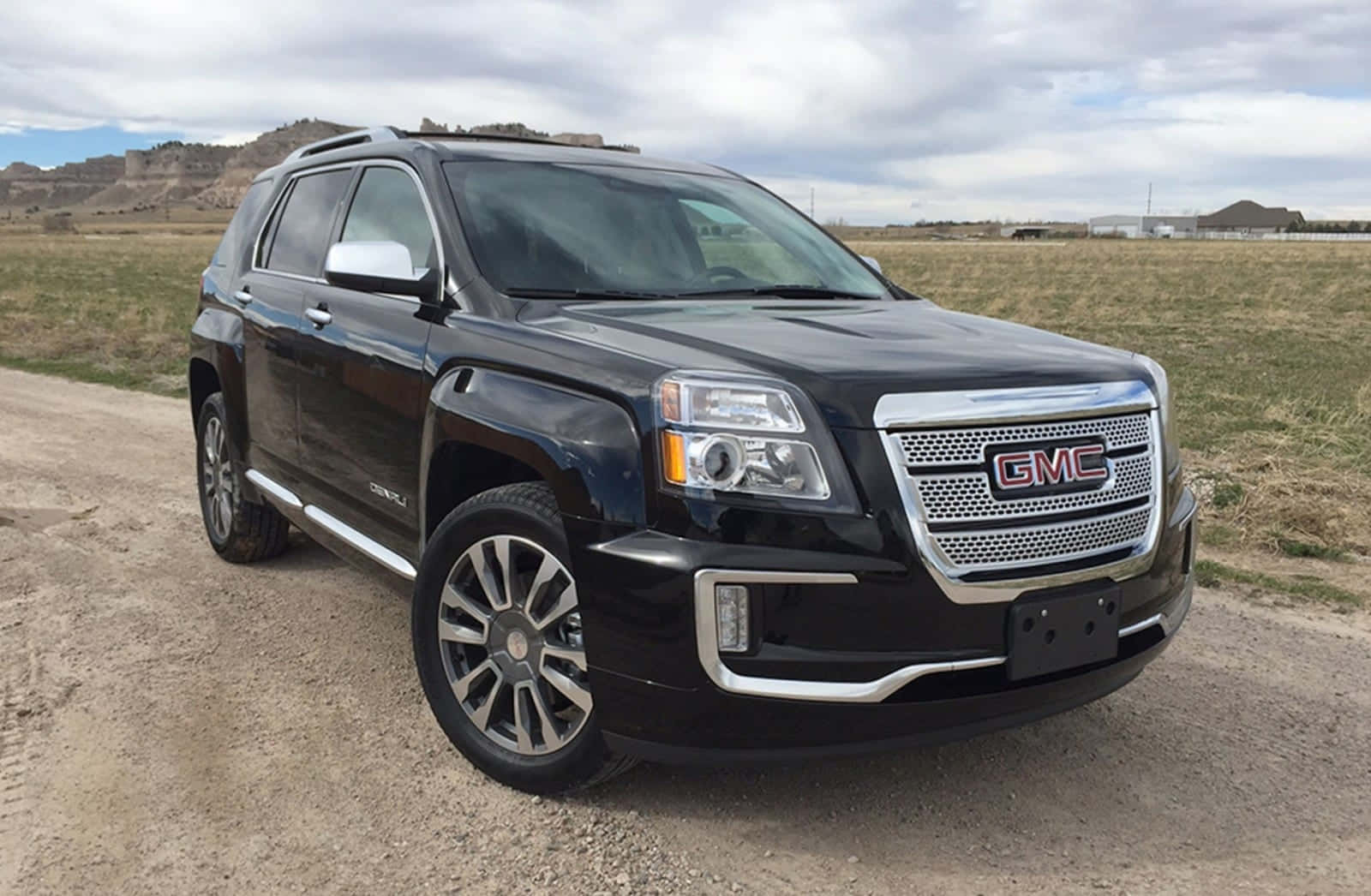 Gmc Terrain 桌布 壁紙 — 一輛時尚的黑色GMC Acadia SUV停泊在碎石路上，背景是起伏的草地山丘和多雲的天空。