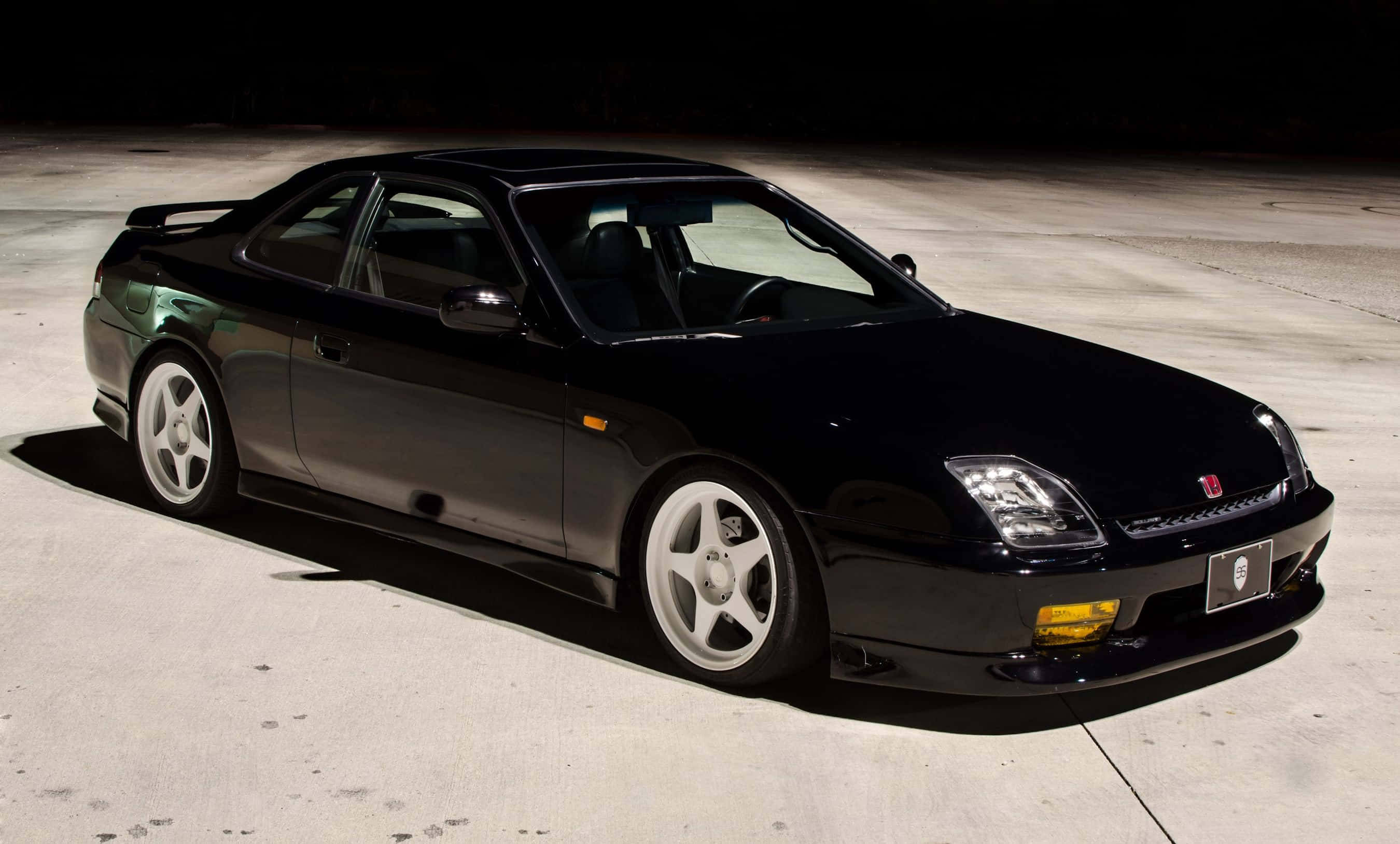 Honda Prelude 桌布 壁紙 — 一輛時尚的黑色本田NSX跑車在攝影棚燈光下，在混凝土車道上閃耀，帶有戲劇性的陰影。