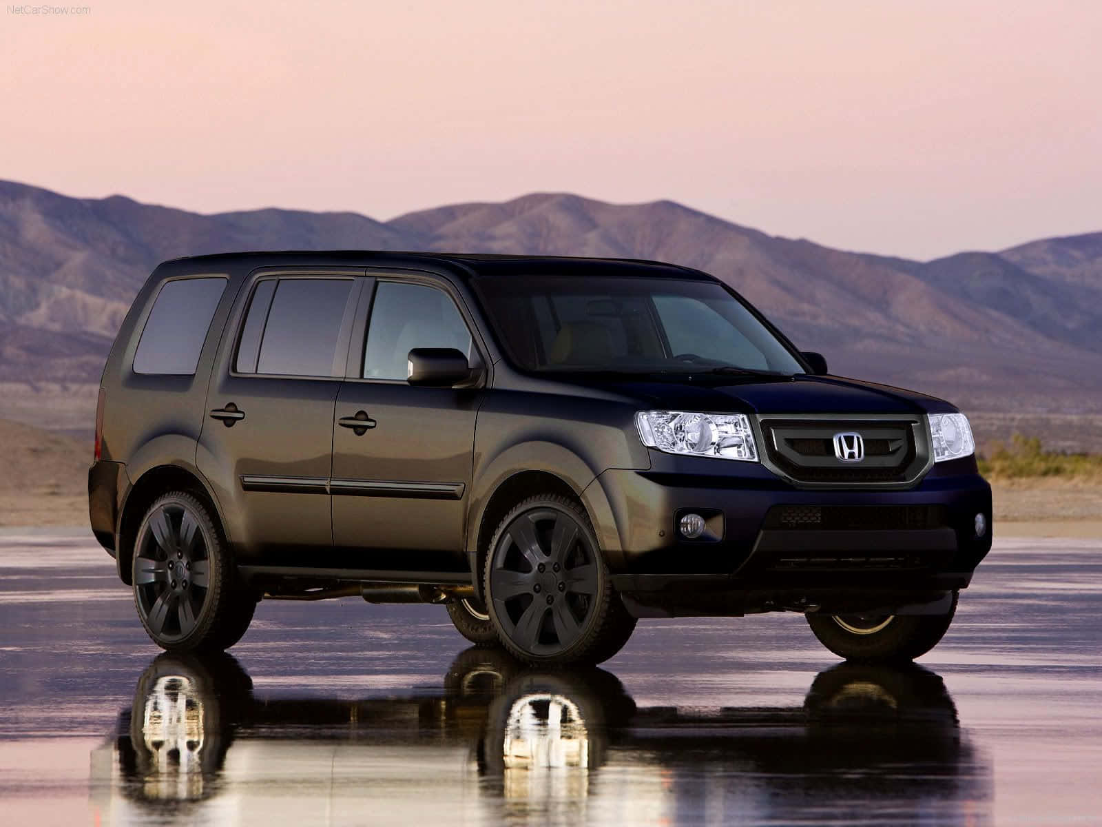 Honda Pilot 桌布 壁紙 — 一輛時尚的黑色本田SUV在濕漉漉的路面上倒映，背景是遠山和柔和的粉紅色日落天空。