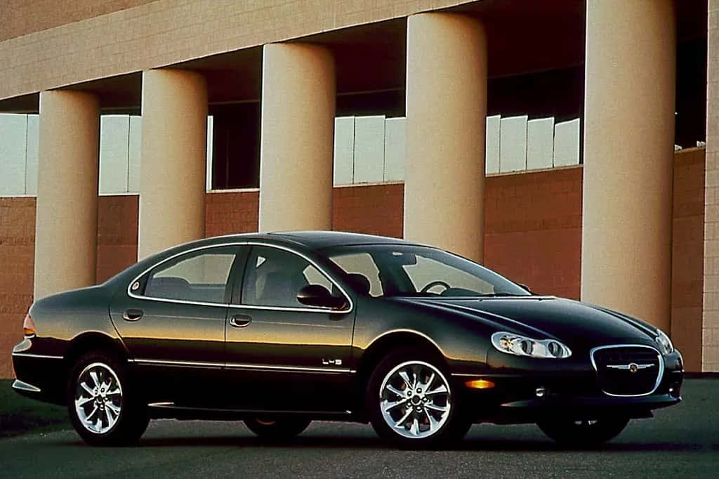 Chrysler Lhs 桌布 壁紙 — 一輛時尚的黑色積架S-Type房車在日光下閃閃發光，停在一棟帶有米色柱子的現代建築前。