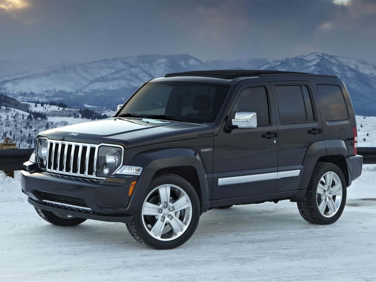 Jeep Liberty 桌布 壁紙 — 一架時尚的黑色Jeep Liberty停在積雪的路邊，白雪覆蓋的山脈在陰沉的暮色天空下若隱若現。