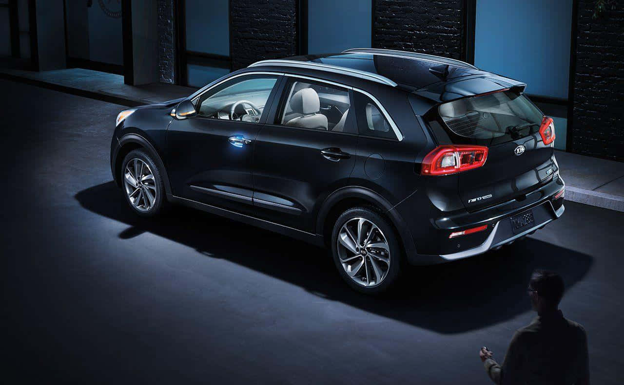 Kia Niro 桌布 壁紙 — 一輛時尚的黑色Kia Niro SUV在戲劇性的工作室燈光下展示，一個剪影人物從下方觀察它。