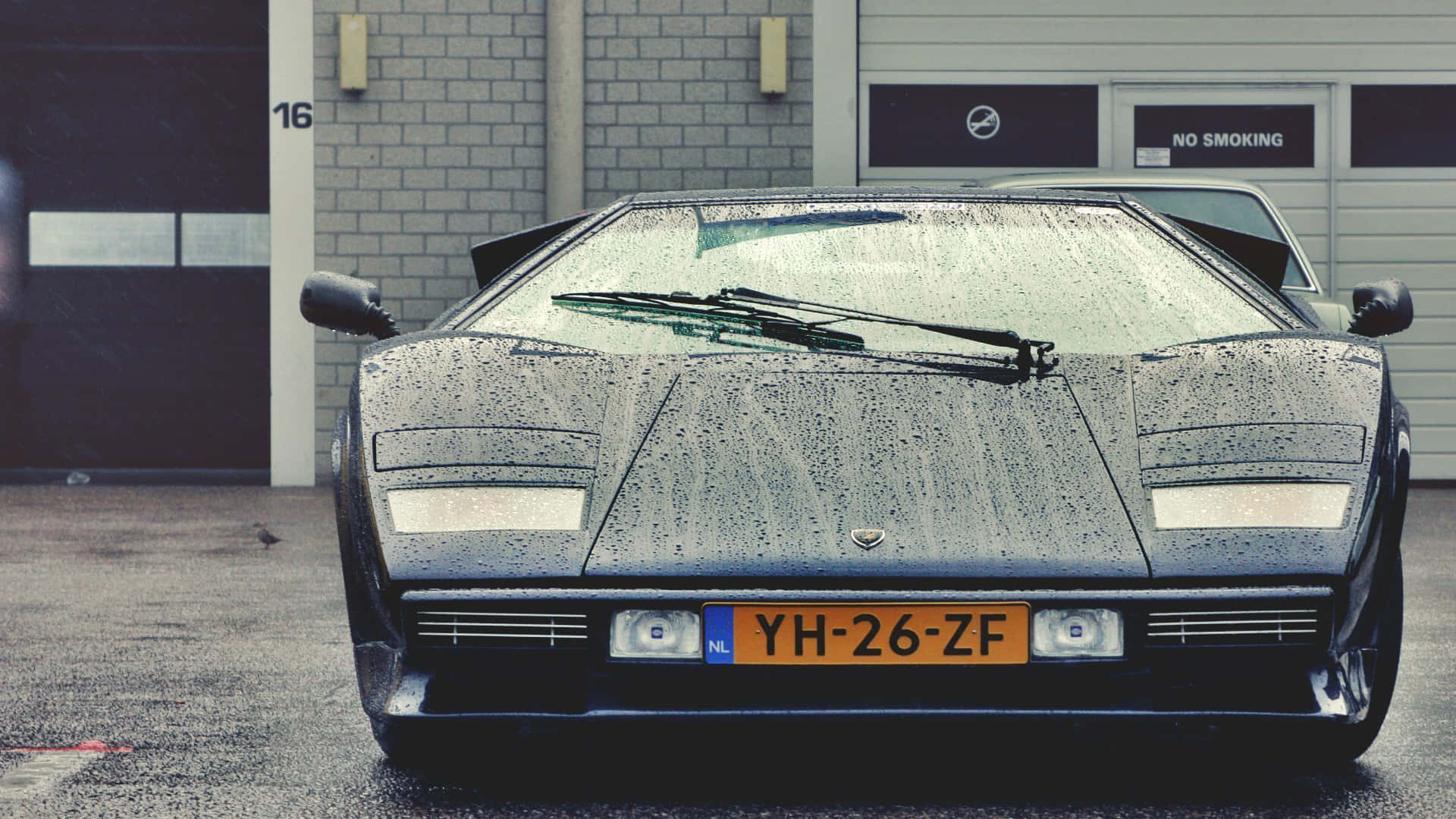 Lamborghini Countach 桌布 壁紙 — 一架流線型黑色林寶堅尼Countach停泊在車庫前，雨滴在其標誌性的棱角車身上閃閃發光。