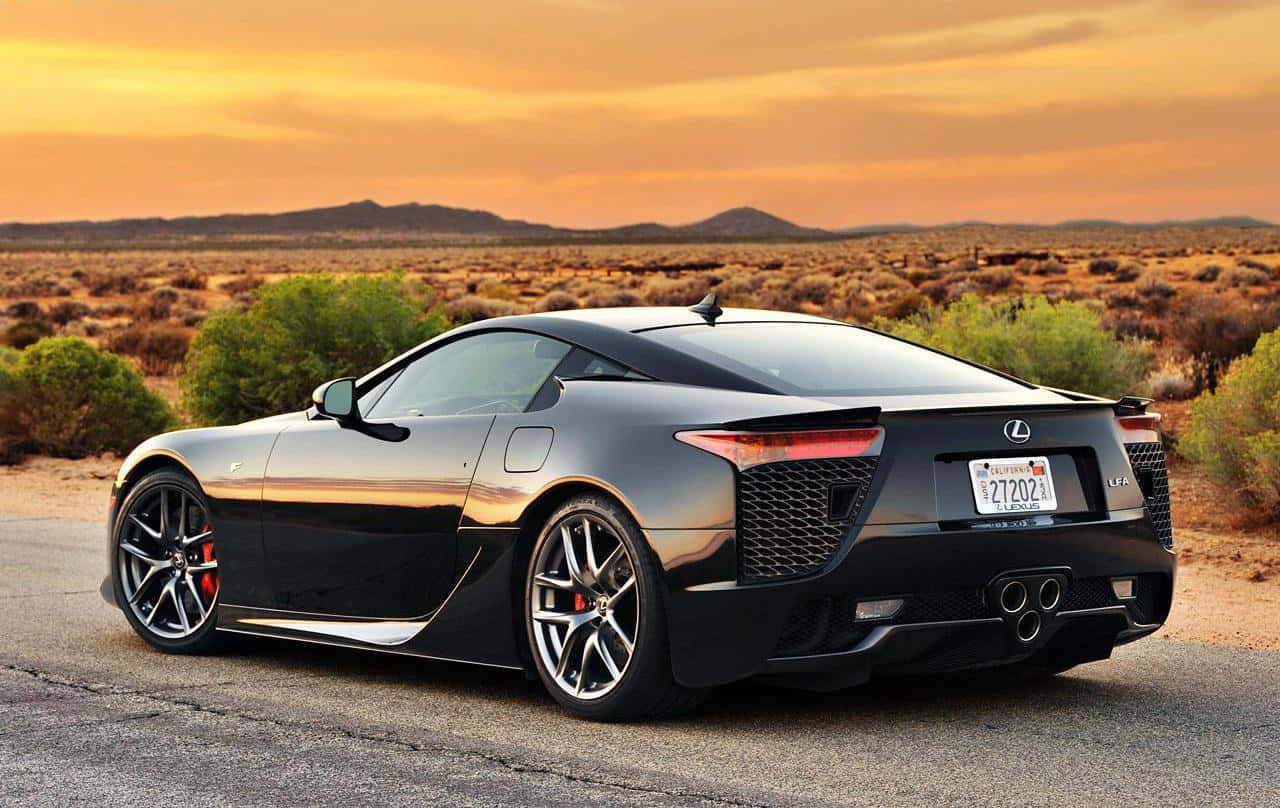 Lexus Lfa 桌布 壁紙 — 一輛時尚的黑色凌志跑車停泊在沙漠公路上，夕陽西下，天空金黃，遠山連綿。