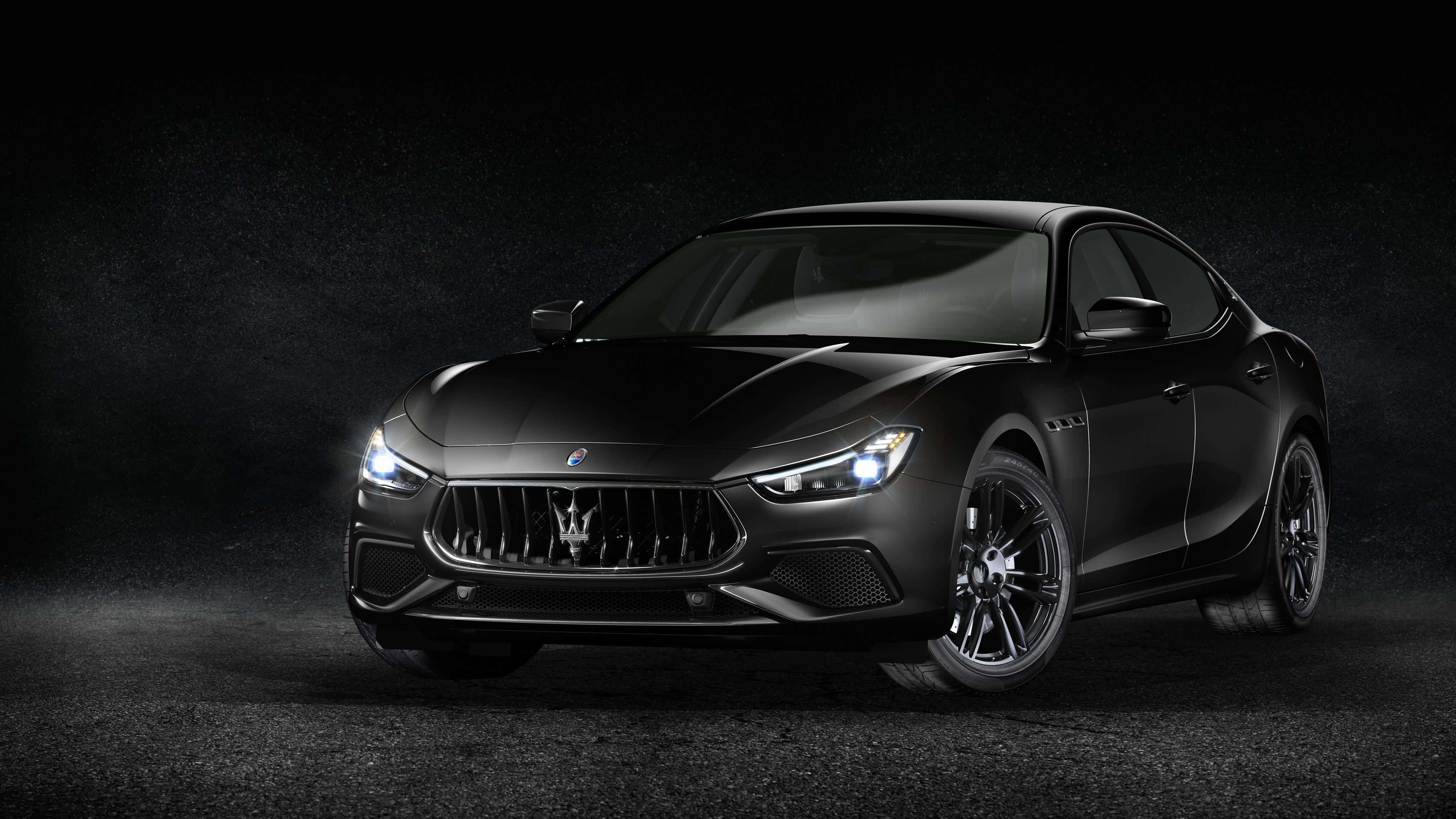 Maserati Ghibli 桌布 壁紙 — 一輛時尚的黑色瑪莎拉蒂跑車在戲劇性的聚光燈下，在深色紋理工作室背景前閃耀。