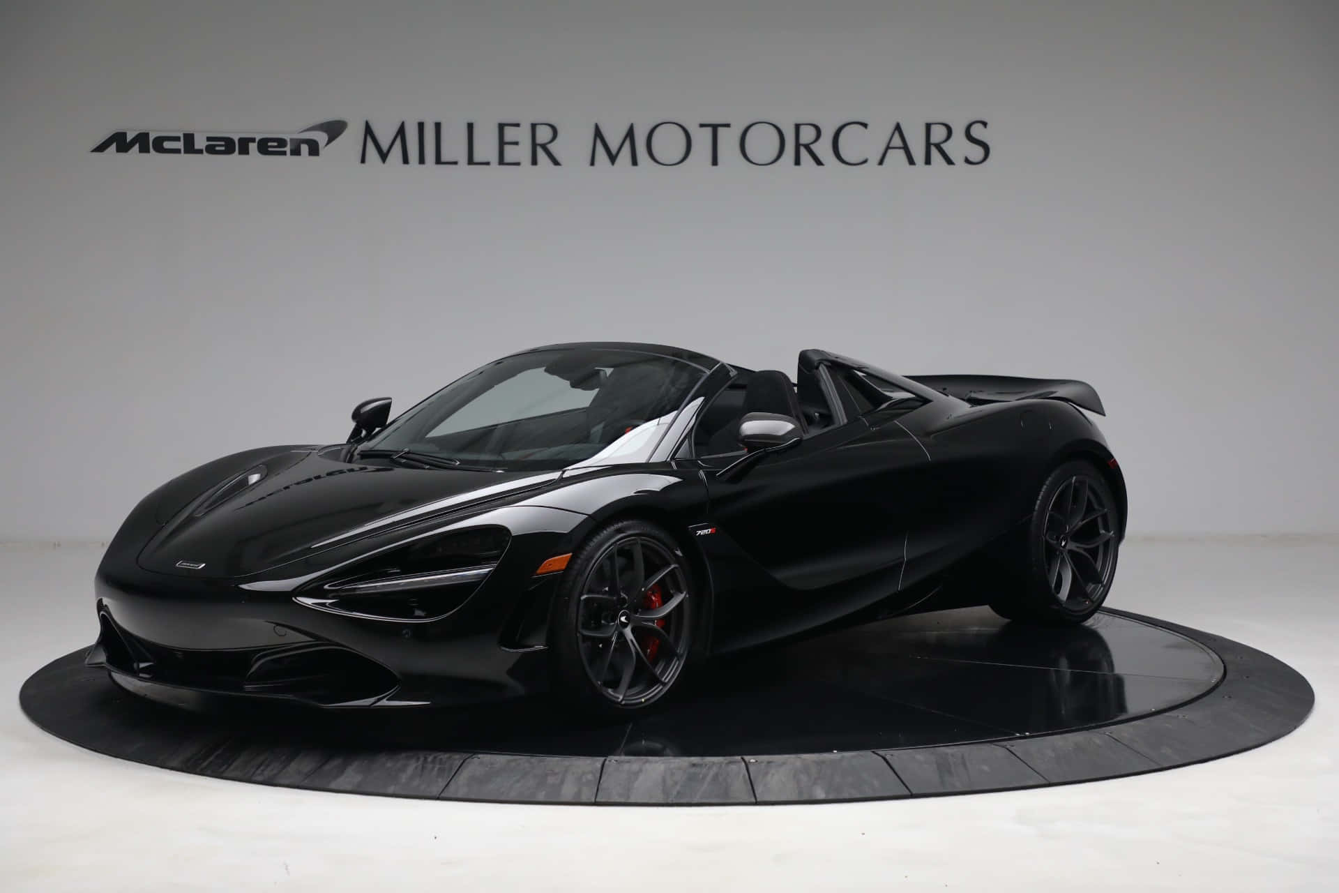 Mclaren 720s Spider 桌布 壁紙 — 一輛流線型黑色McLaren 720S Spider開篷跑車在圓形展示台上於攝影棚燈光下閃閃發光。