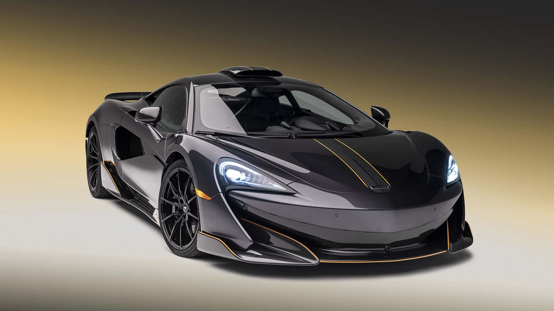 Mclaren 600lt 桌布 壁紙 — 一輛時尚的黑色McLaren跑車，帶有金色裝飾和發光車頭燈，擺放在黃色漸變背景前。
