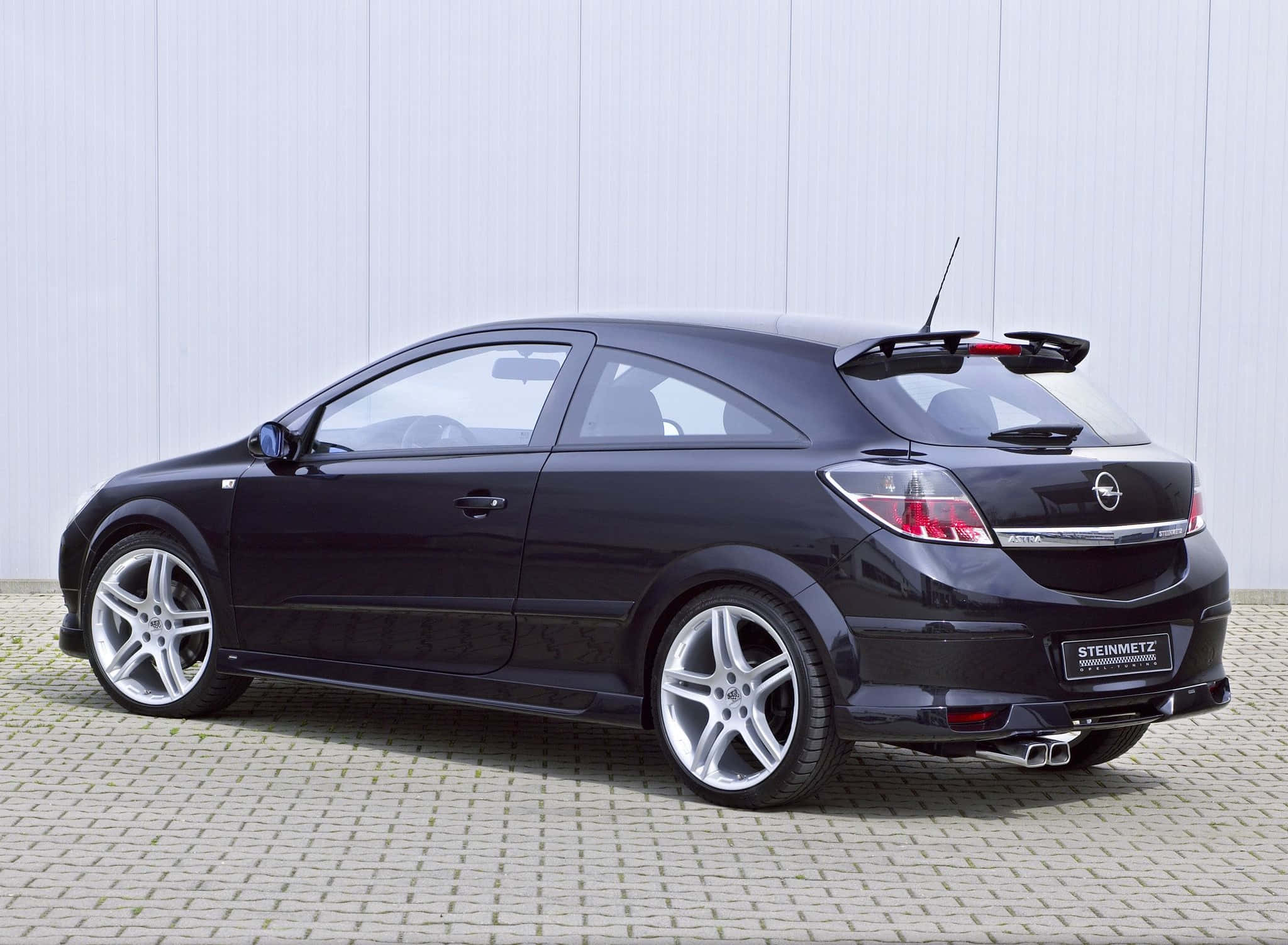 Opel Astra 桌布 壁紙 — 一架型格黑色改裝Opel Astra GTC跑車，停泊在鋪砌路面上，背景為淺灰色牆壁。